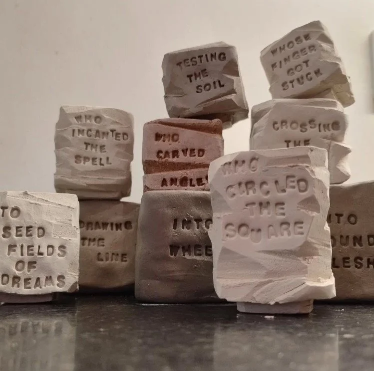 A stack of small square unfired clay pots with lines of a poem pressed into them. The pots are various clay colours and have been carved into around the sides and corners.