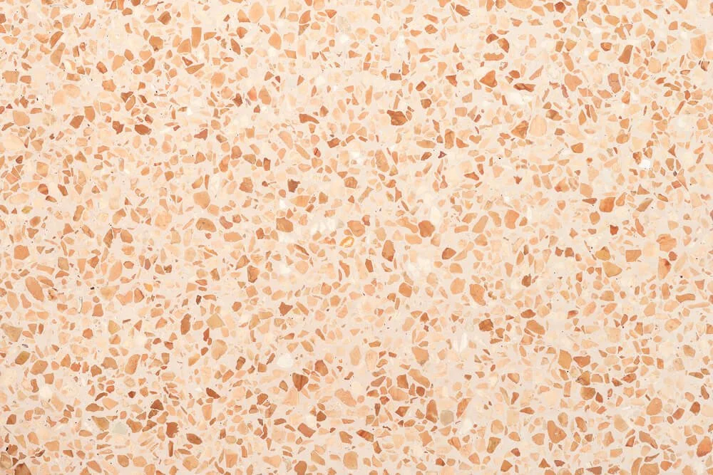 Surface en terrazzo beige clair avec petits morceaux de pierre rose et orange.
