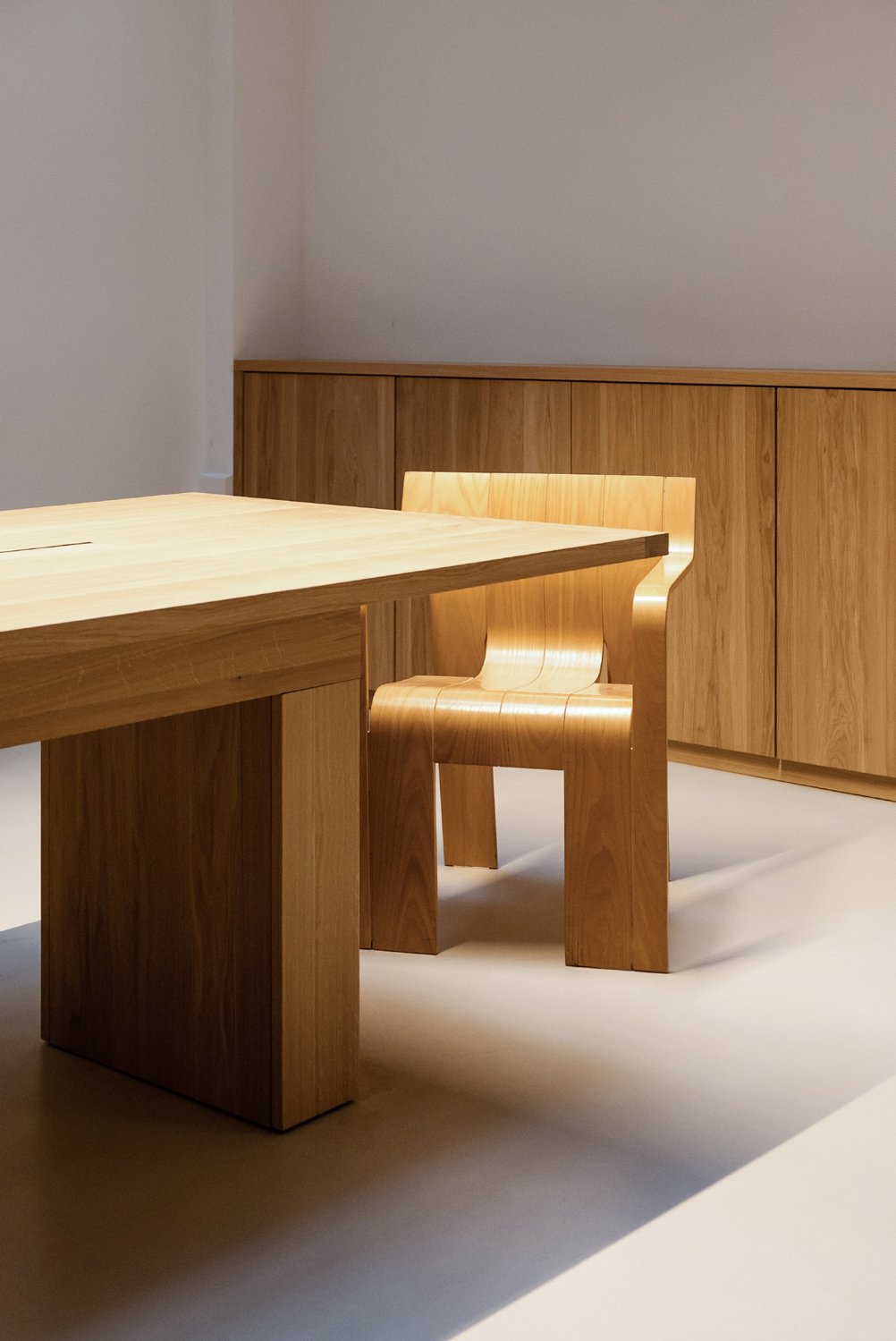 Une table et une chaise en bois clair avec un meuble en bois derrière, dans une pièce avec murs blancs