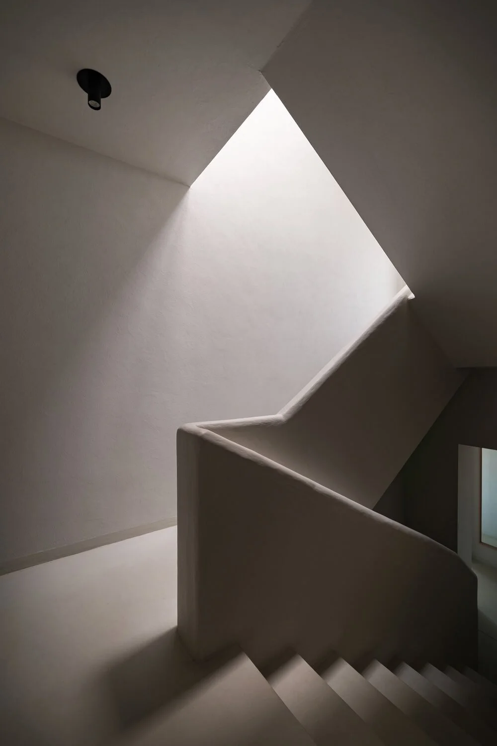 Escalier intérieur avec mur blanc et ouverture en forme de carré au plafond laissant entrer la lumière