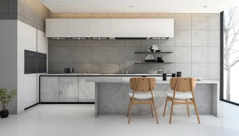 Cuisine moderne avec mur en béton, comptoir en marbre, armoires blanches, deux chaises en bois et une grande fenêtre avec vue sur des arbres.