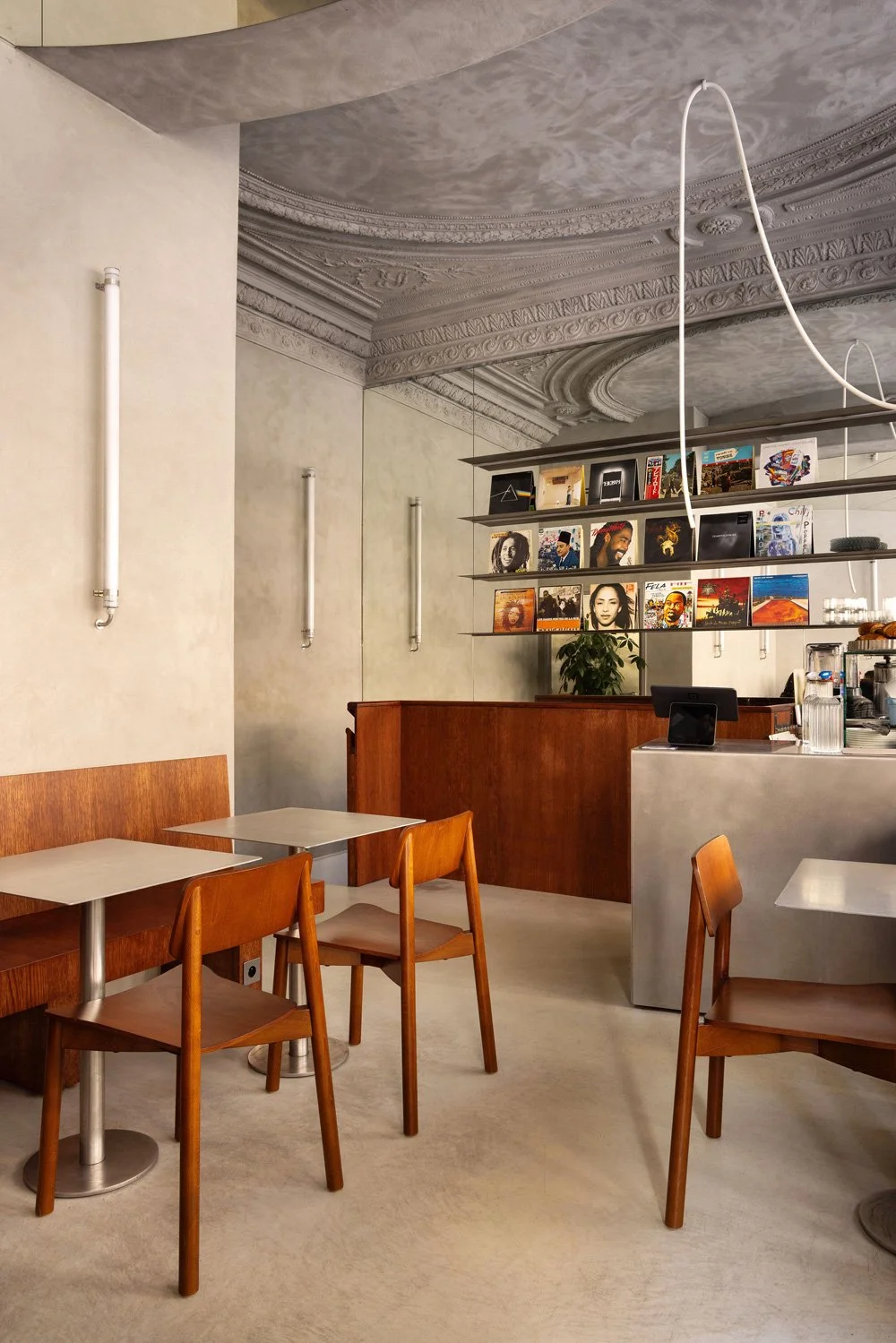Intérieur d'un café avec tables en bois, chaises, étagère en suspension avec des disques vinyles, comptoir, et décor ancien au plafond.