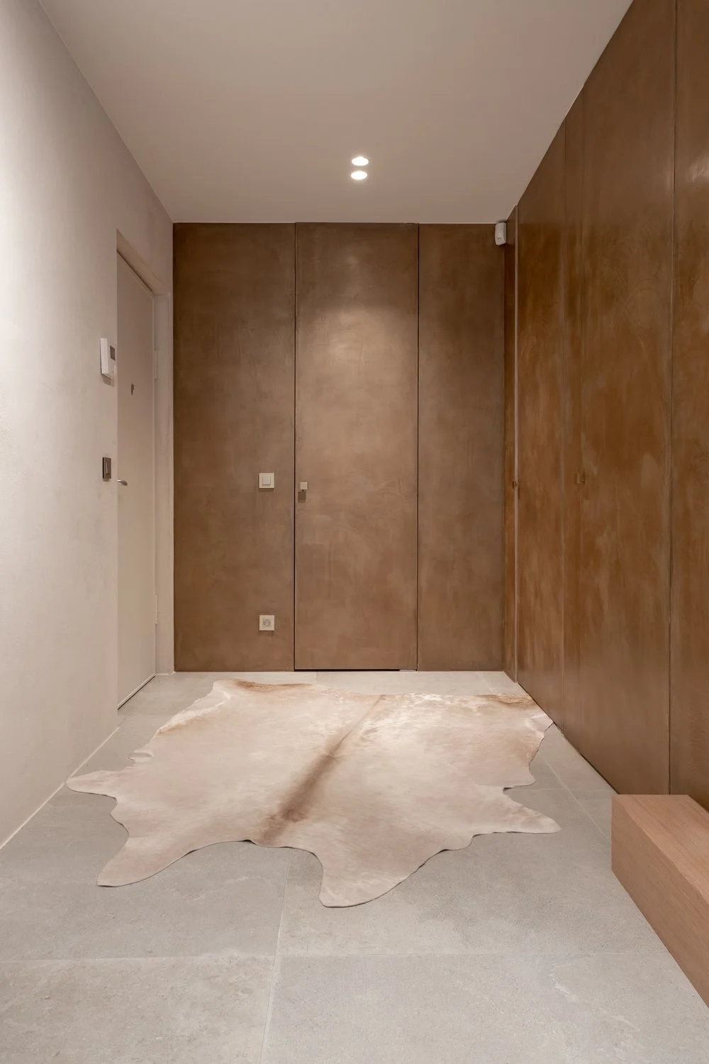 Hall d'entrée moderne avec mur en bois, sol en carreaux clairs, tapis en peau de vache, porte d'entrée en blanc, éclairage encastré au plafond.