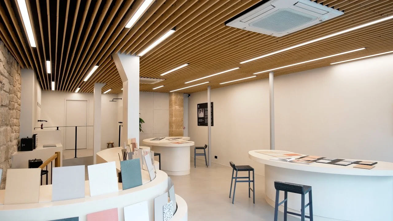 Espace intérieur moderne avec comptoirs ovales, chaises, murs blancs, plafond en bois avec éclairage intégré, et une architecture mélangeant pierre et matériaux contemporains.