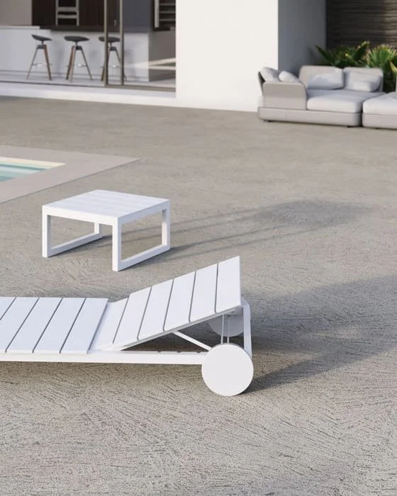 Mobilier de piscine blanc comprenant une chaise longue et une table, à côté d'un espace avec un salon extérieur et un jardin.