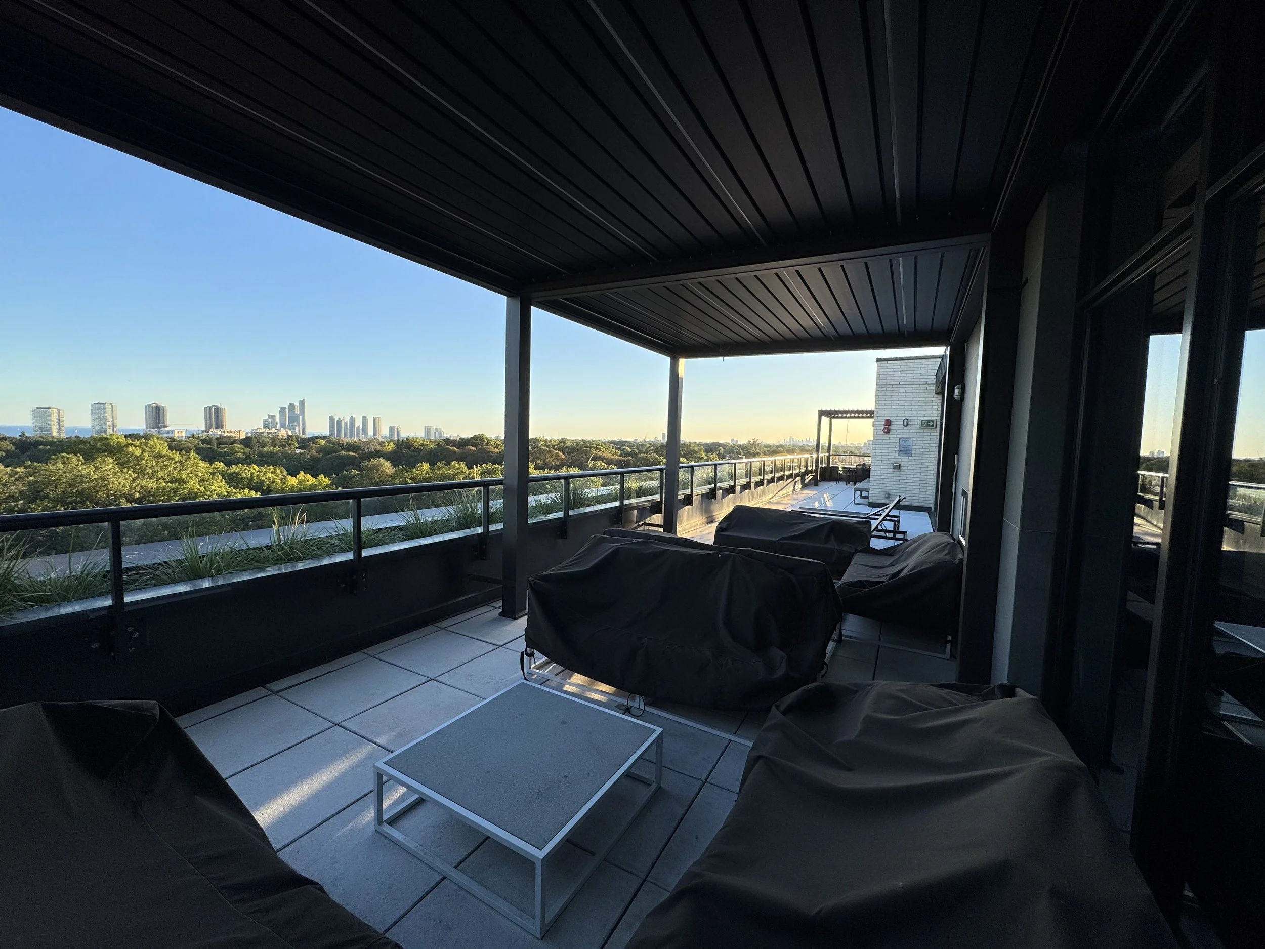 Balcony with patio furniture overlooking a city skyline with multiple high-rise buildings and a large green park area in the foreground.