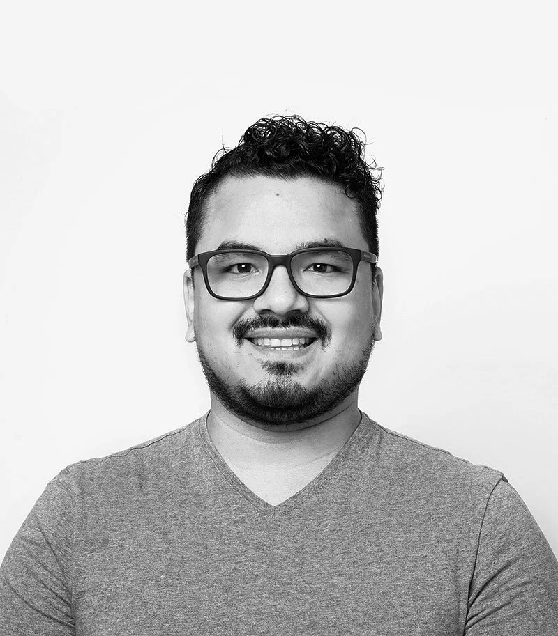 Andrés Sánchez smiling with glasses and a beard, wearing a V-neck T-shirt, standing against a white background.
