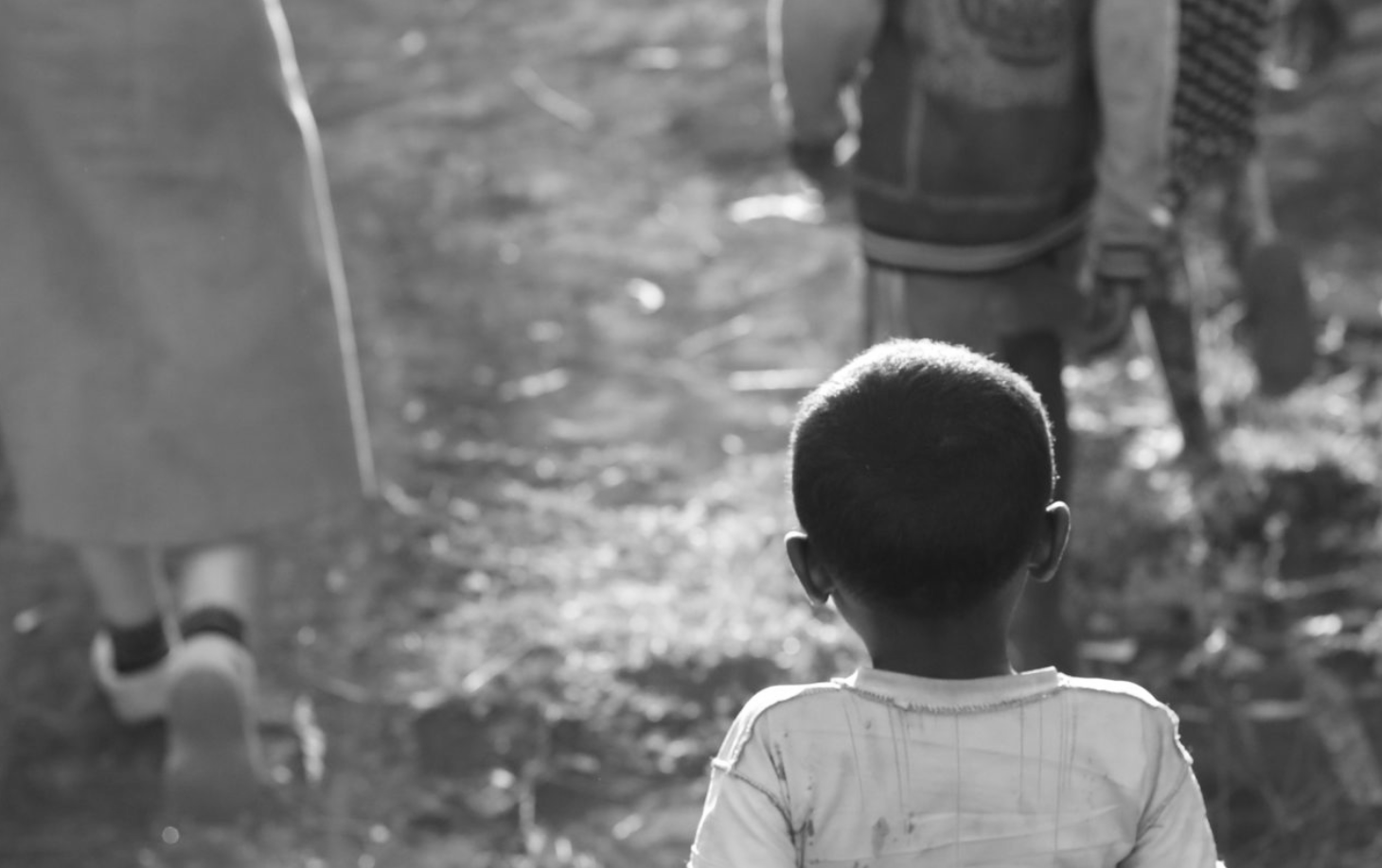 Back view of a young boy with short hair, walking outdoors with others, in black and white.