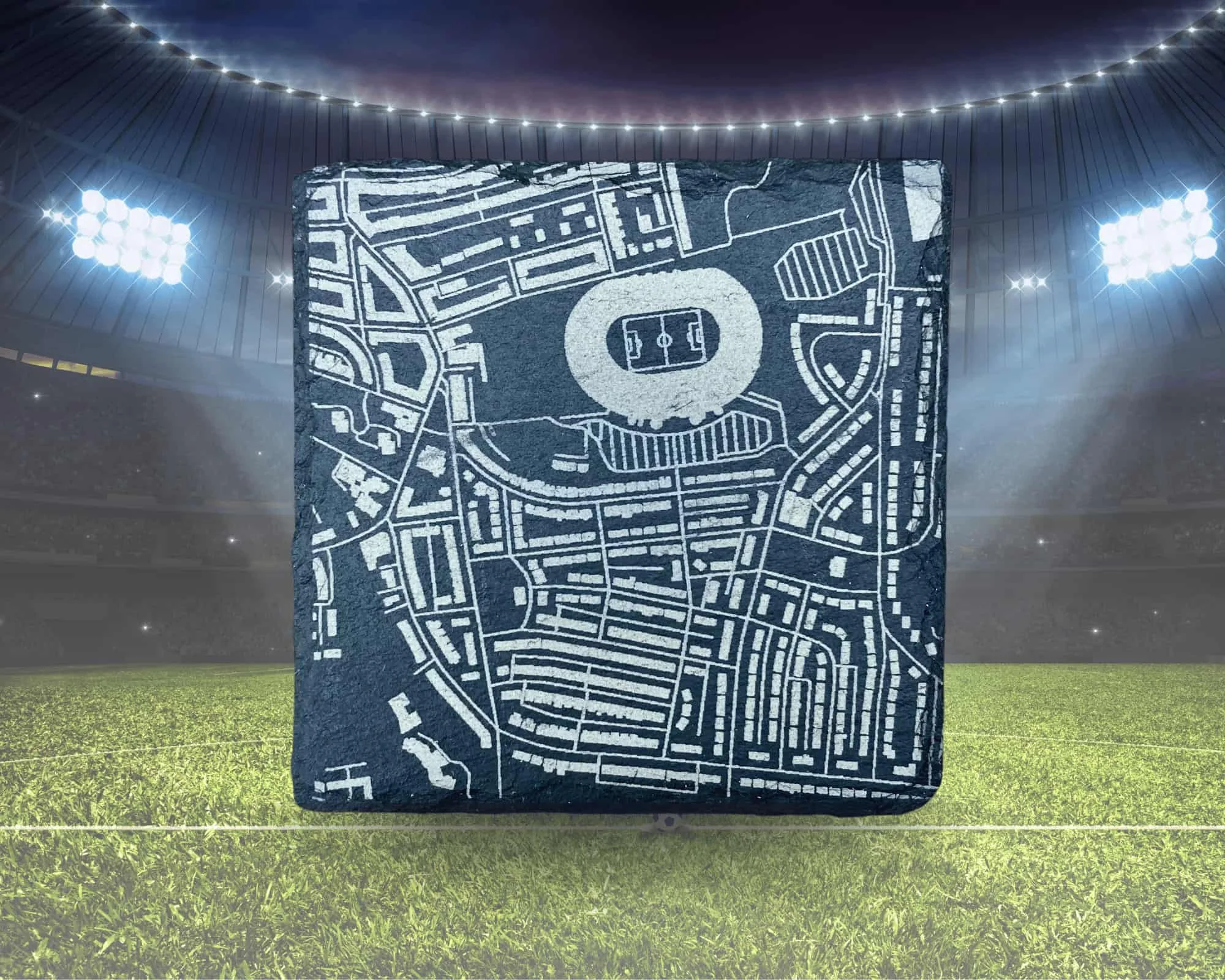 A large stone with a map of a soccer stadium carved into it, situated in a soccer stadium with bright floodlights and a grassy field.