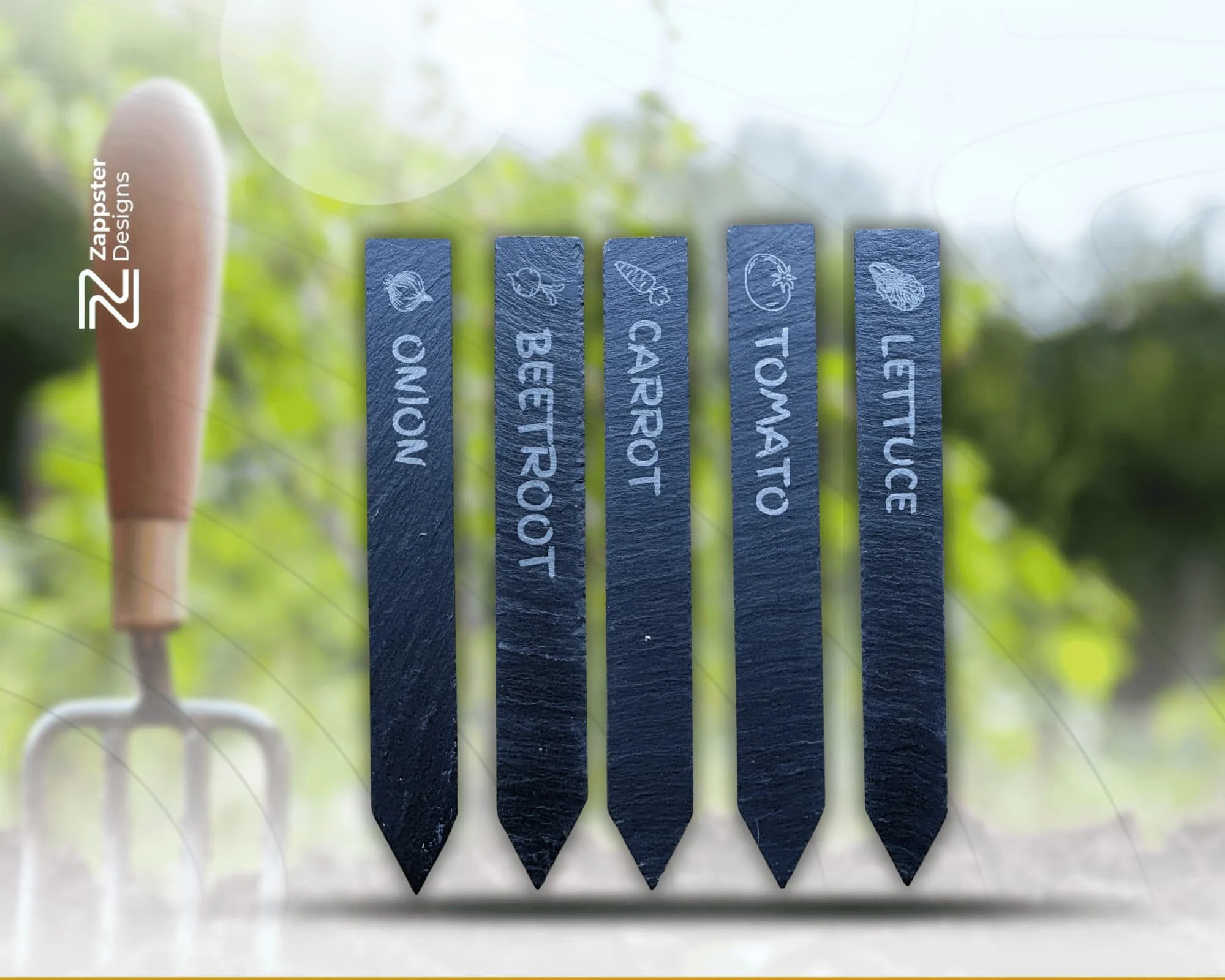 Close-up of five gardening plant markers labeled 'ONION,' 'BEETROOT,' 'CARROT,' 'TOMATO,' and 'LETTUCE' with a gardening fork and a blurred garden background.