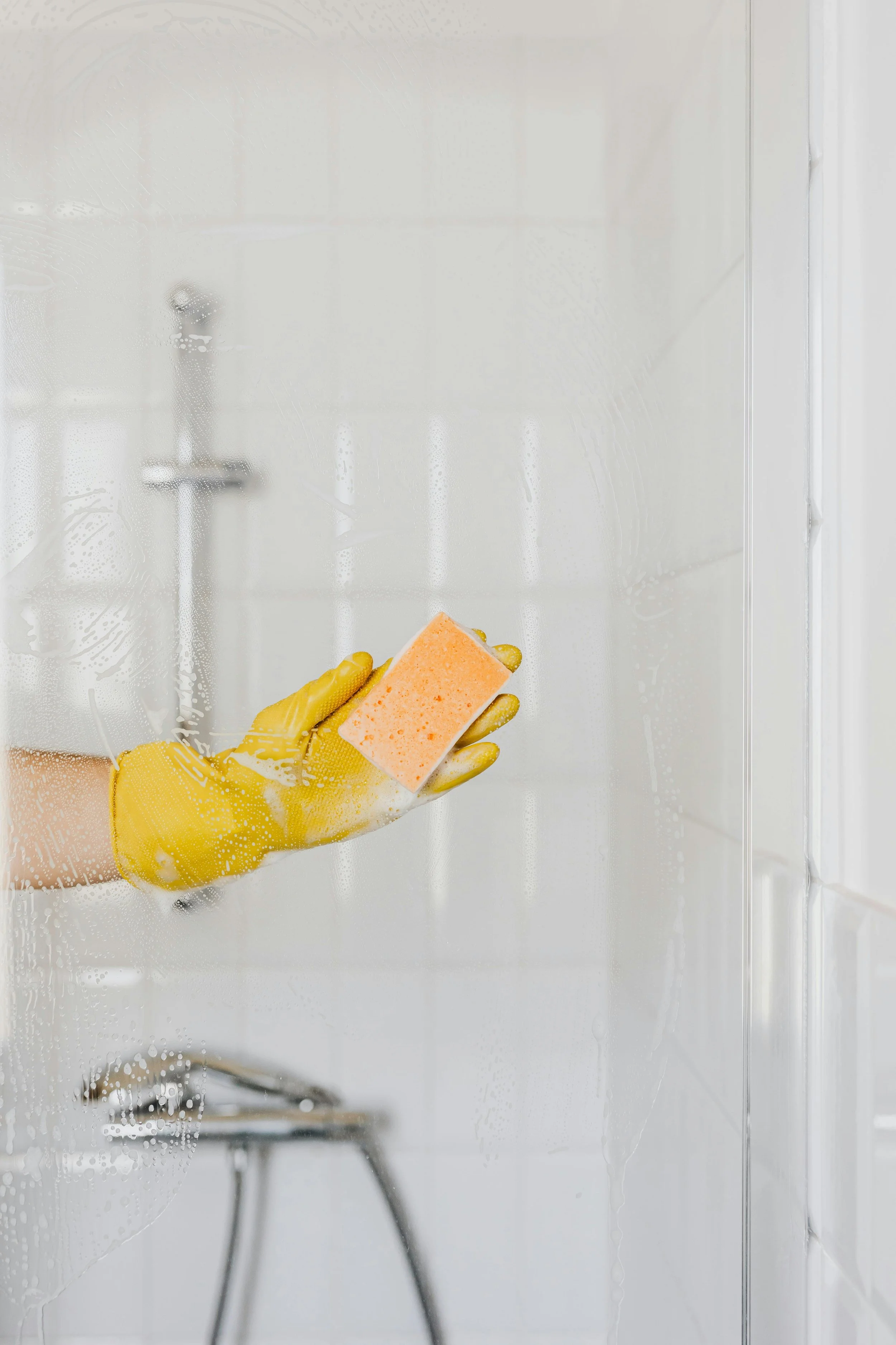Person cleaning a shower glass door with a sponge and yellow gloves.