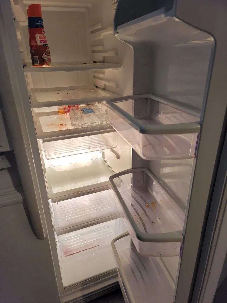 Empty refrigerator with some food stains, a bottle of spray, and a few remaining food containers and items.