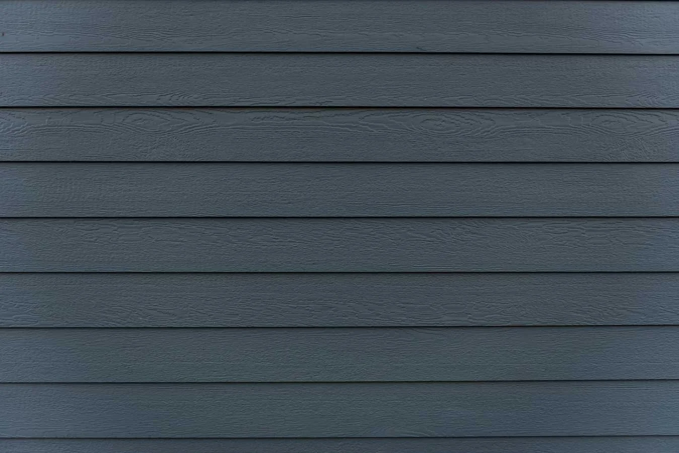 Close-up view of dark gray horizontal fiber cement siding panels on a house exterior, showing a smooth, wood-grain texture and uniform alignment.