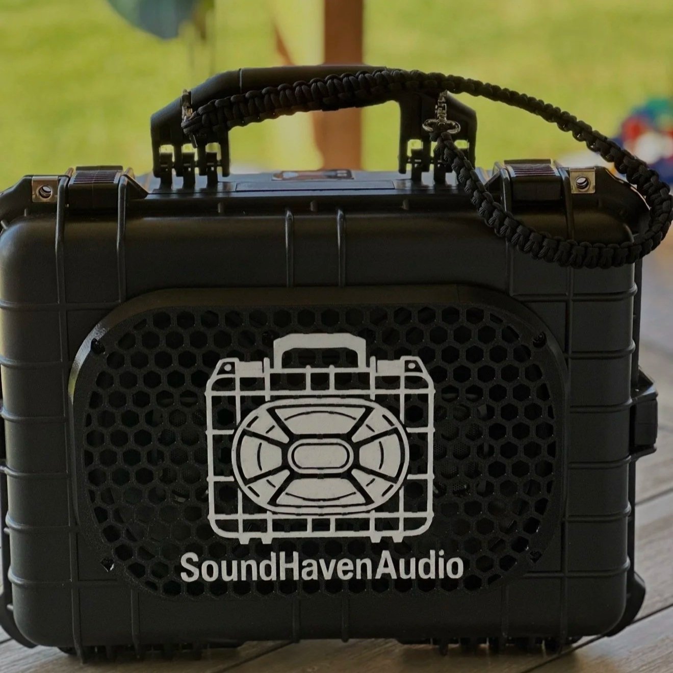 A black portable speaker with a handle, safety lanyard, and a white SoundHavenAudio logo featuring a stylized speaker icon on the front grille.