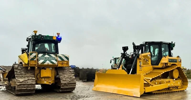 Two large yellow bulldozers on a construction site, one with a blade and the other with a ripper, with cloudy sky in the background.