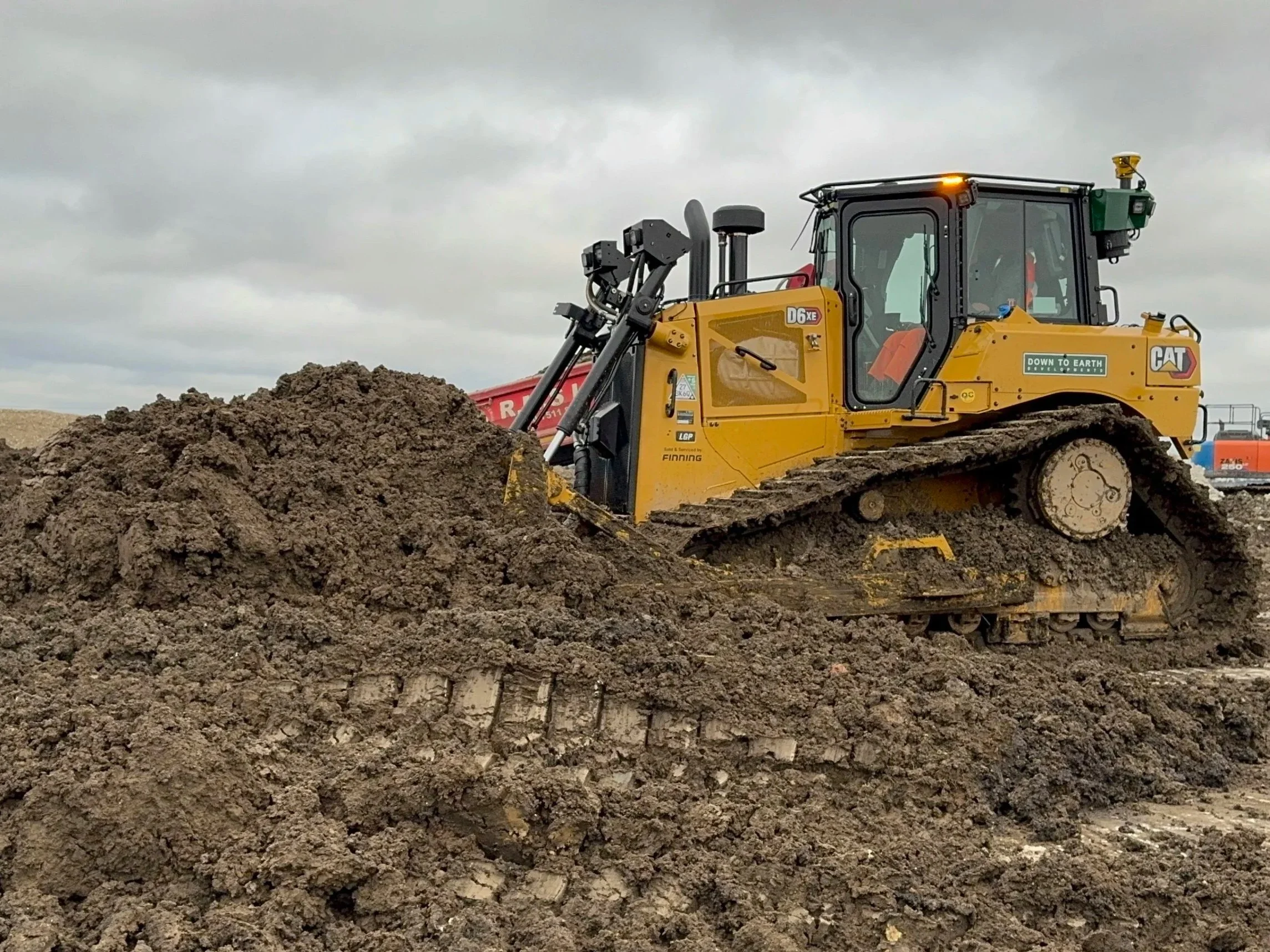 A yellow Caterpillar bulldozer moving dirt on a construction site under a cloudy sky.