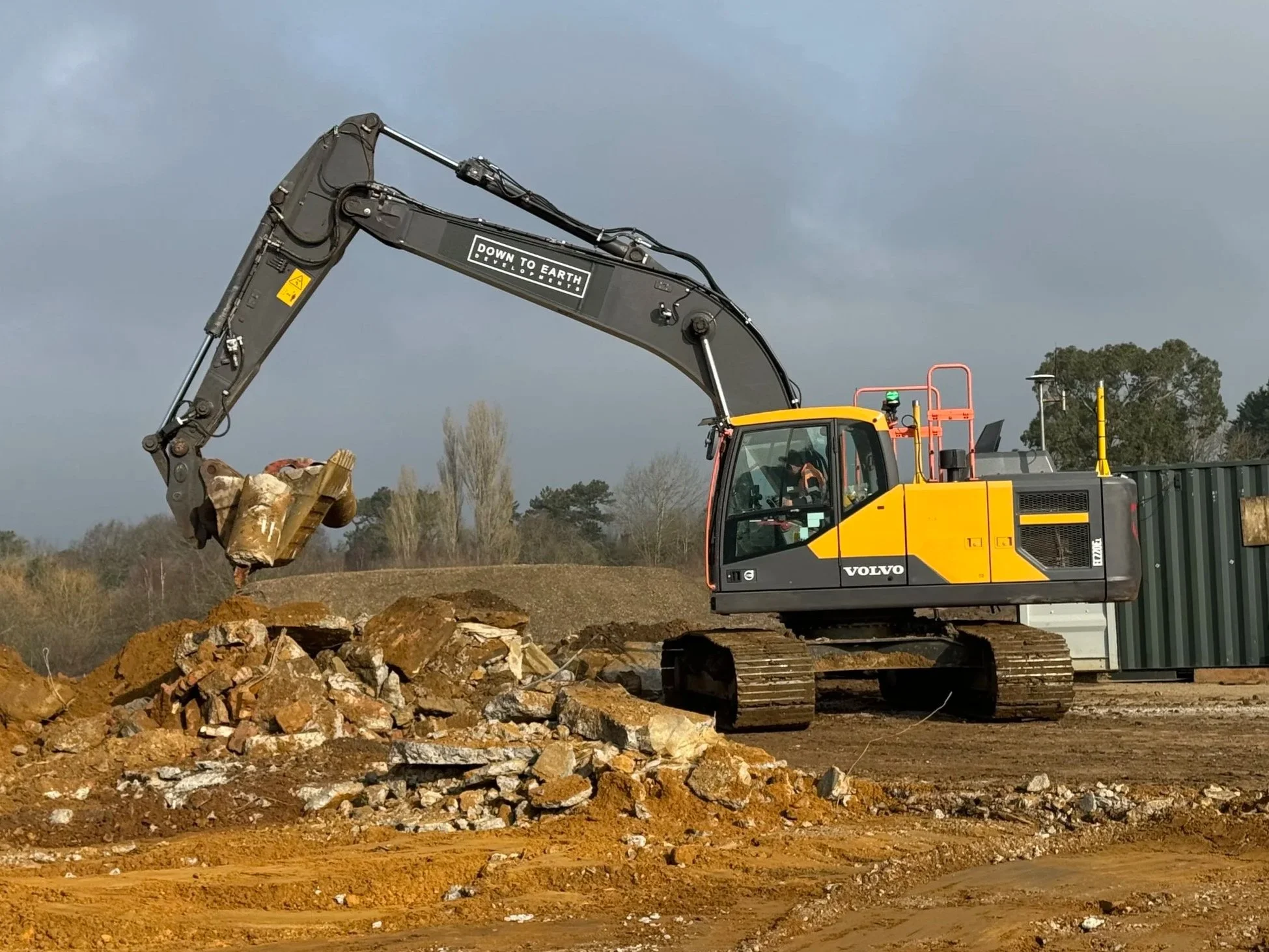A yellow and black Volvo excavator is moving dirt and rocks at a construction site during daytime.