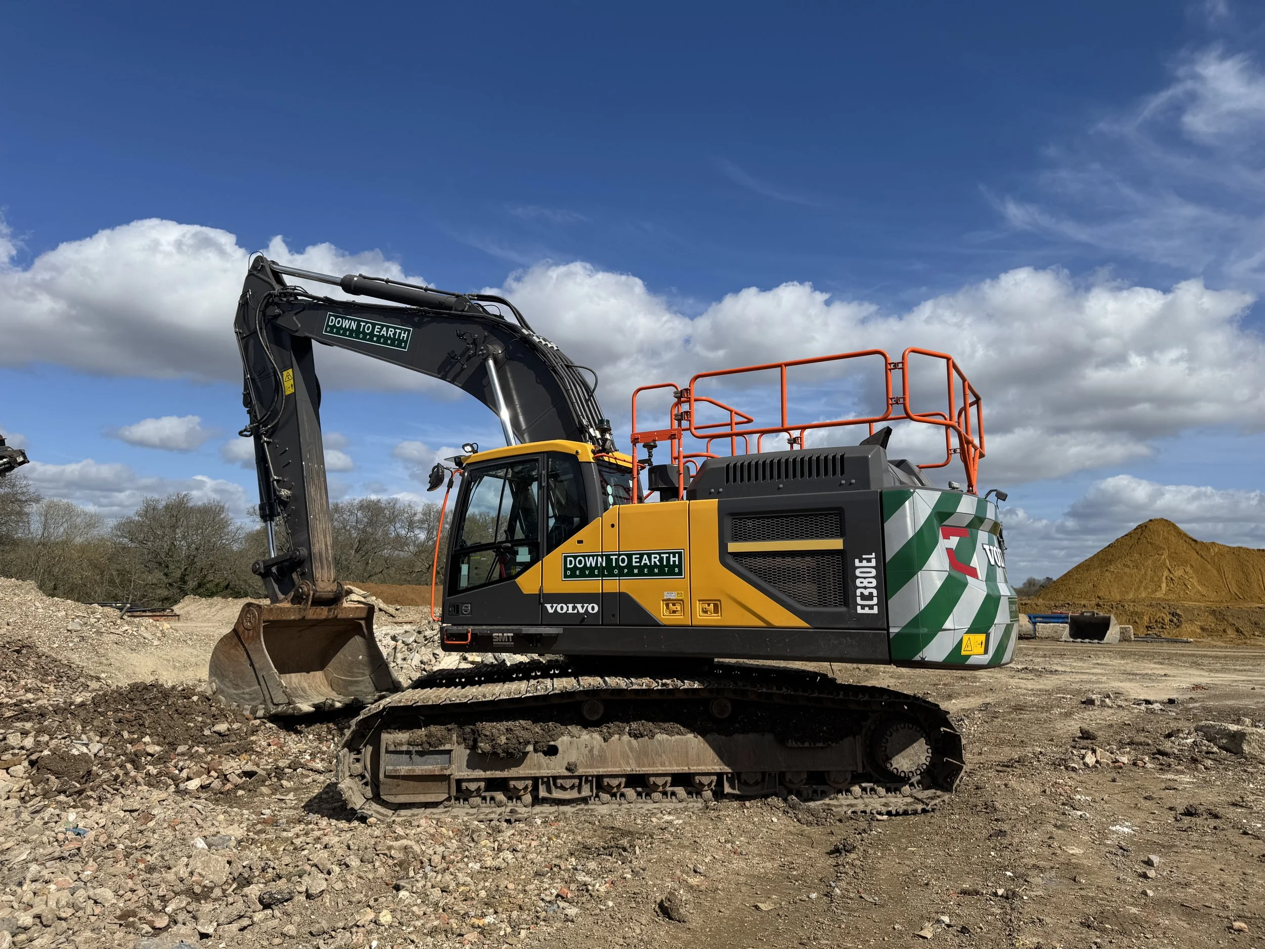 A Volvo excavator on a construction site with a partly cloudy sky overhead.