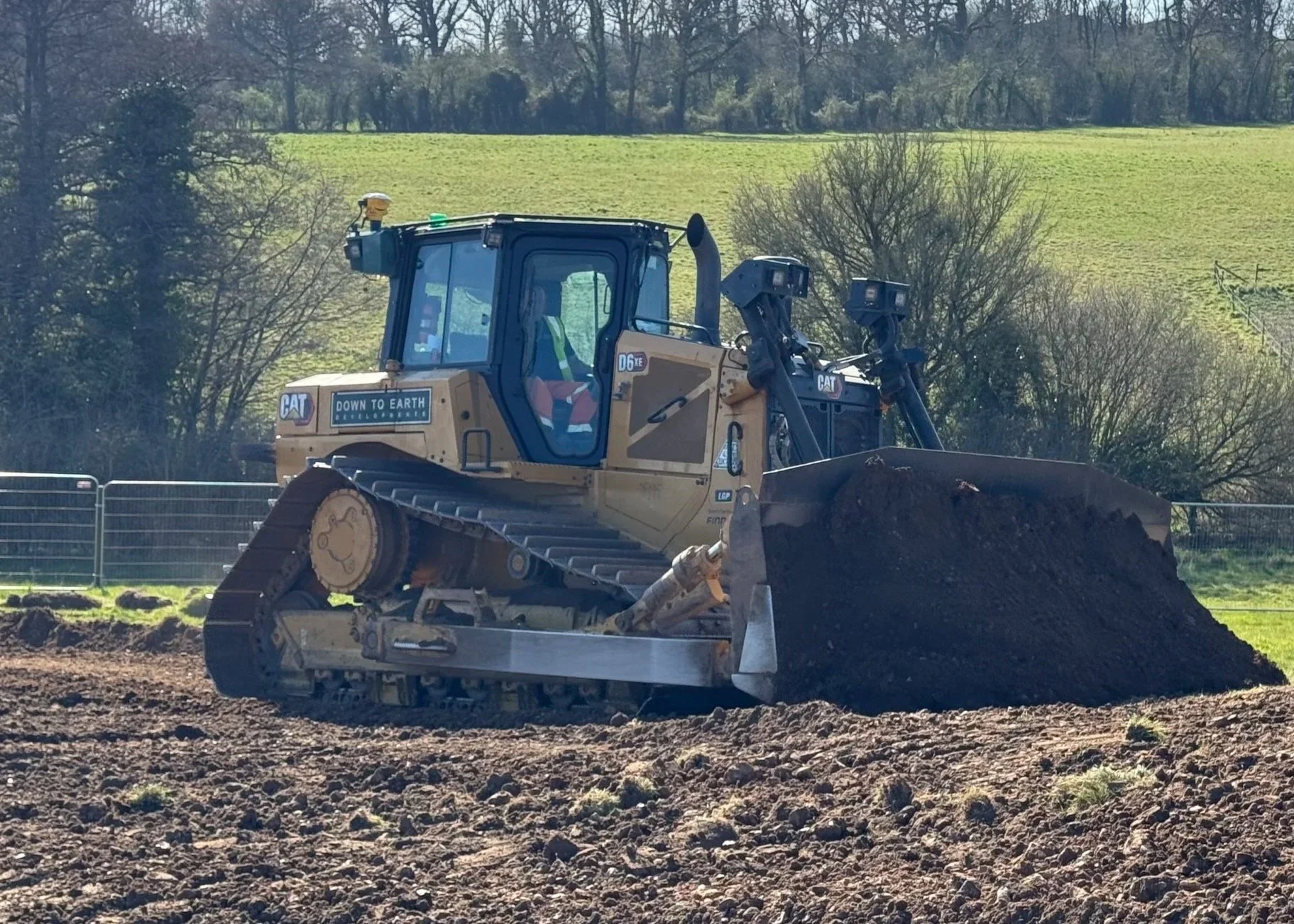 A large CAT bulldozer moving soil on a construction site with green grass and trees in the background.