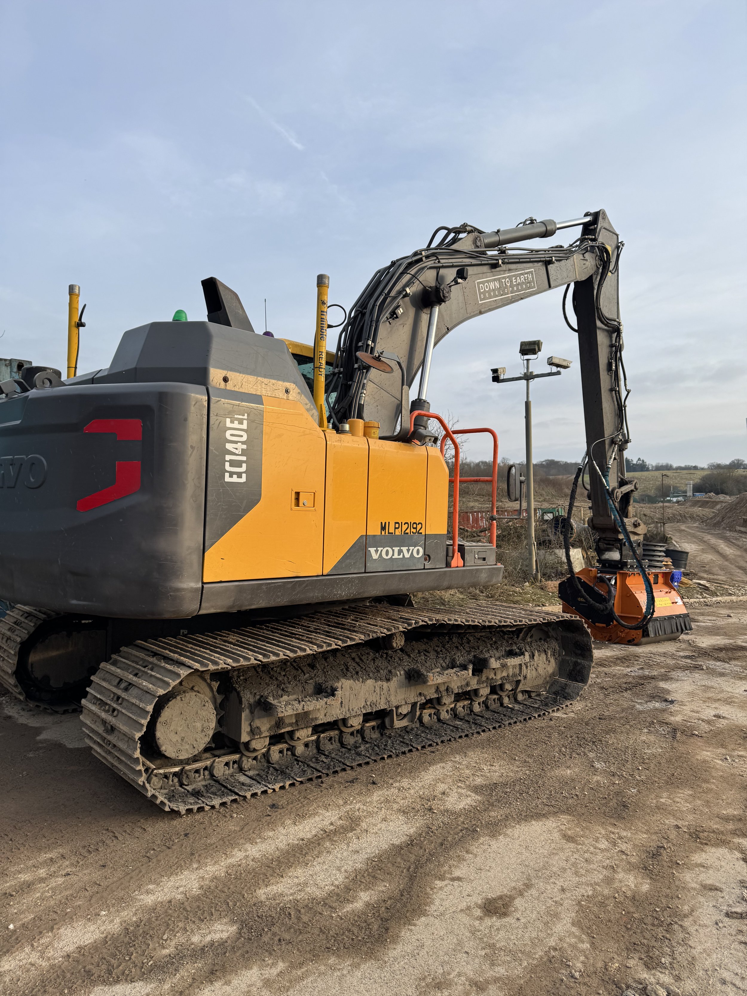 A Volvo EC140EL excavator on a construction site with dirt ground and a clear sky in the background.