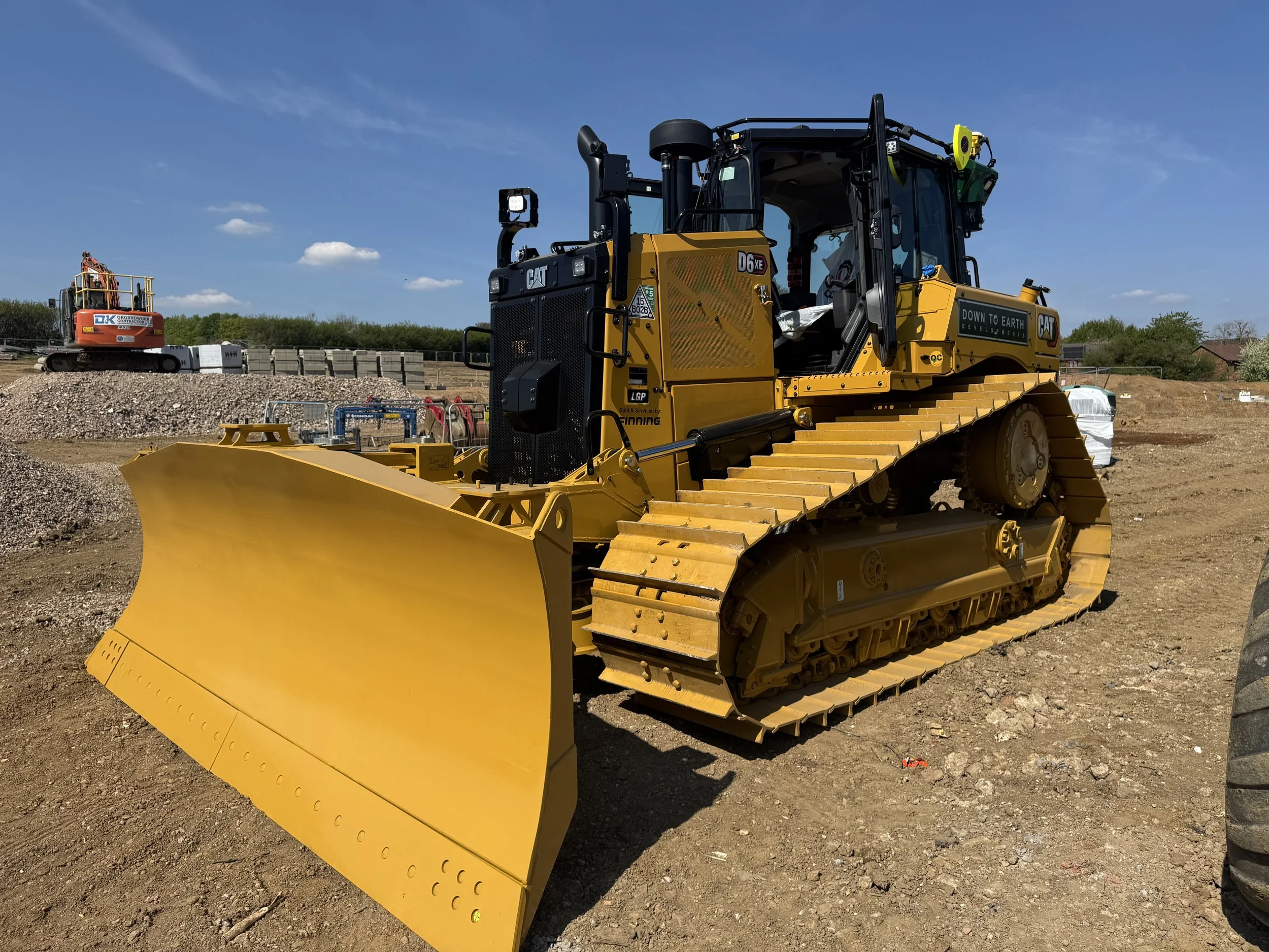 A large yellow bulldozer with a black cab and tracks on a construction site underneath a clear blue sky.