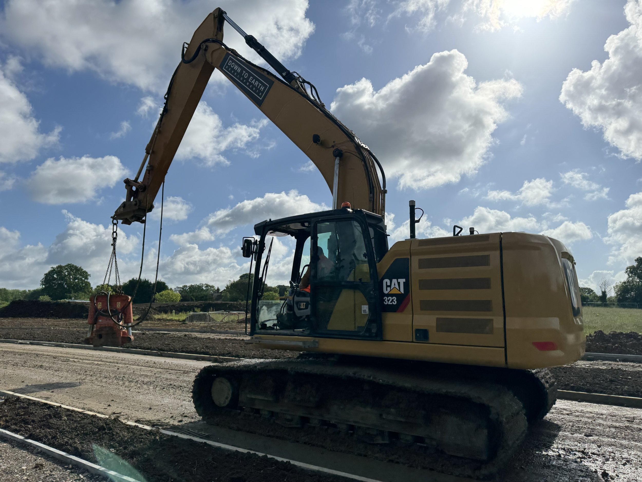 A yellow excavator working on a construction site during daytime with a partly cloudy sky.