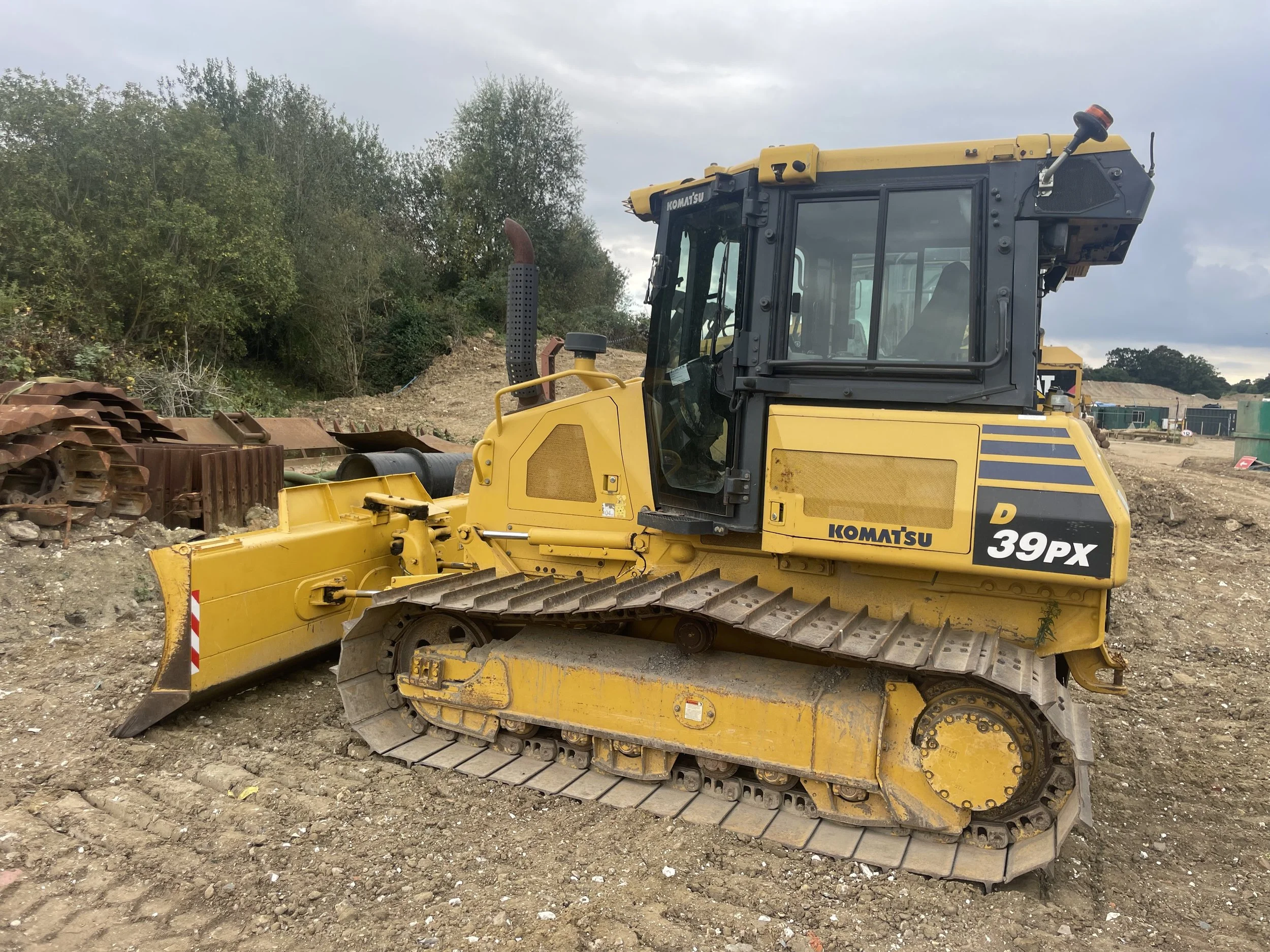 A yellow Komatsu D 39PX bulldozer at a construction site with dirt and trees in the background.