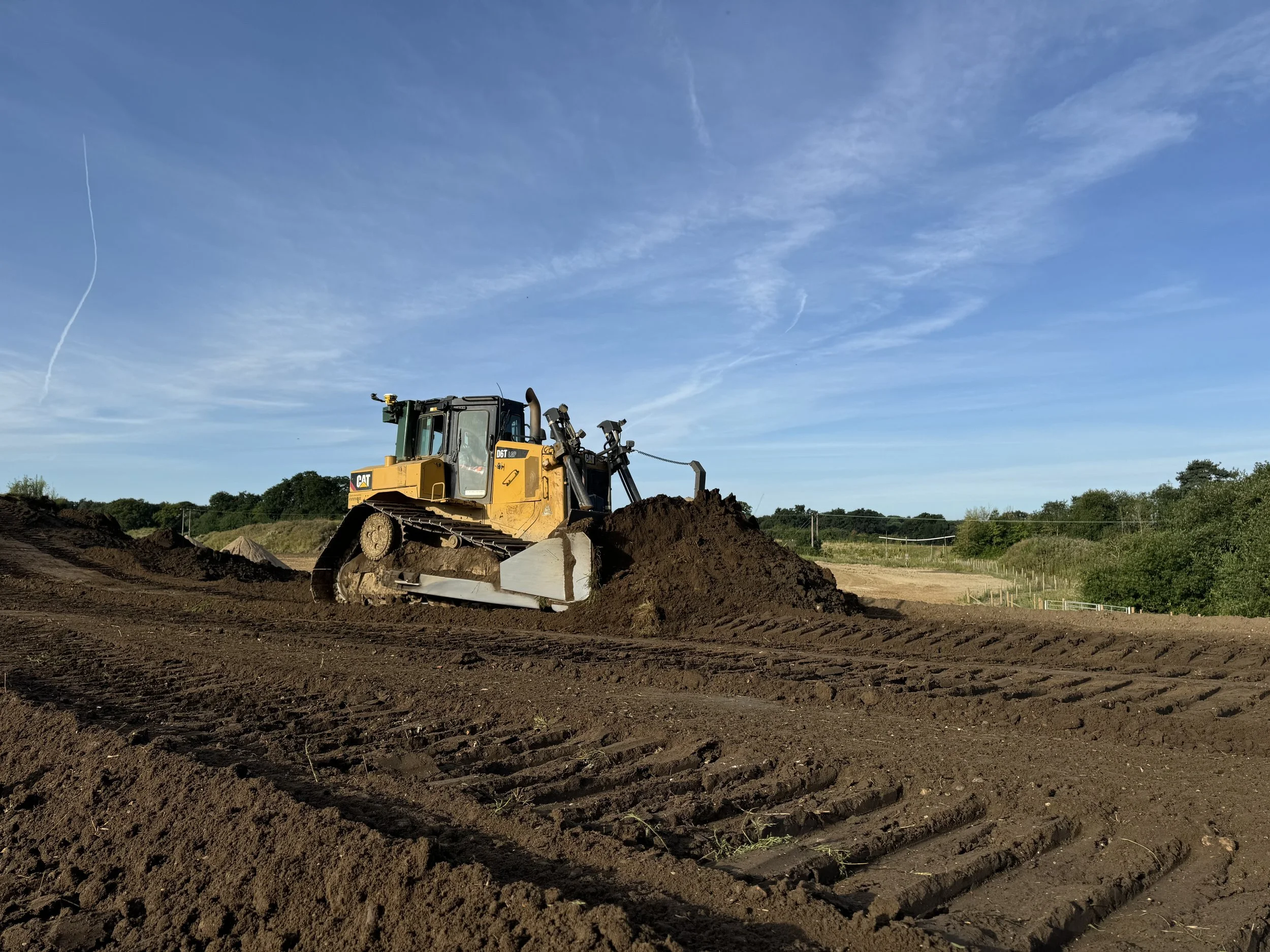 A yellow Caterpillar bulldozer moving dirt on a construction site under a blue sky with wispy clouds.