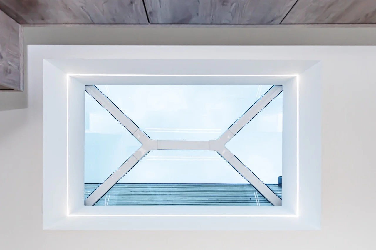View of a skylight ceiling with a modern framing and blue sky outdoors, photographed from inside the building.