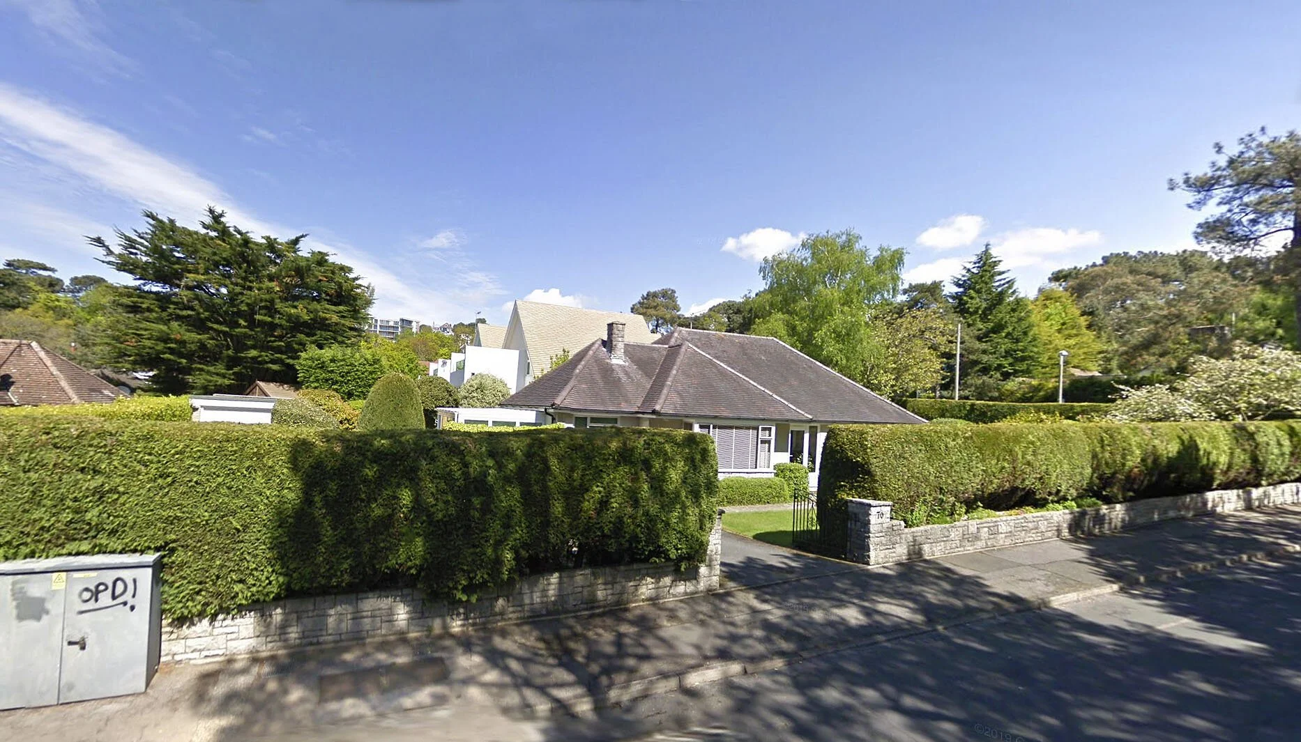 Residential house situated on the South Coast in Poole, Dorset with a hedge front yard, blue sky, and trees in the background.