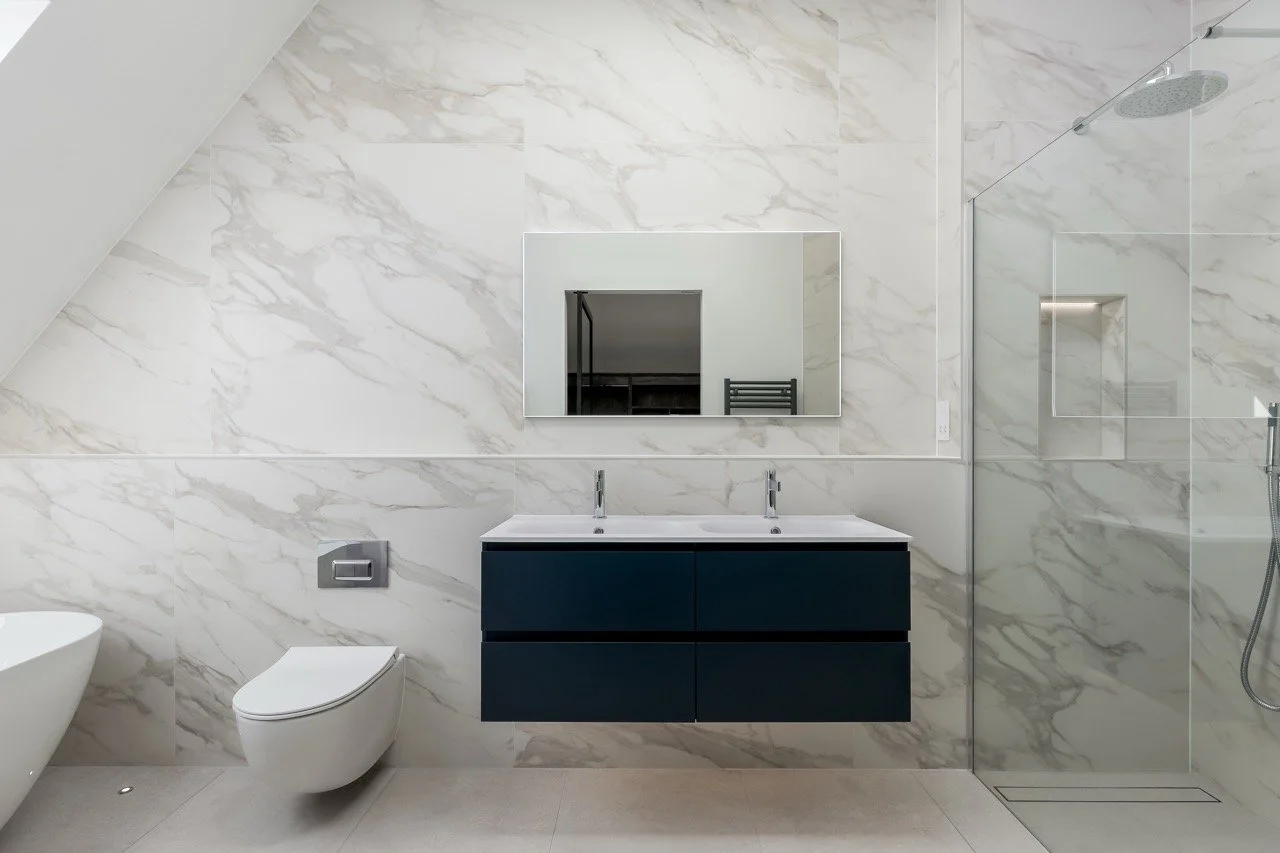 Modern bathroom with marble walls, floating double sink vanity, wall-mounted toilet, and glass-enclosed shower.