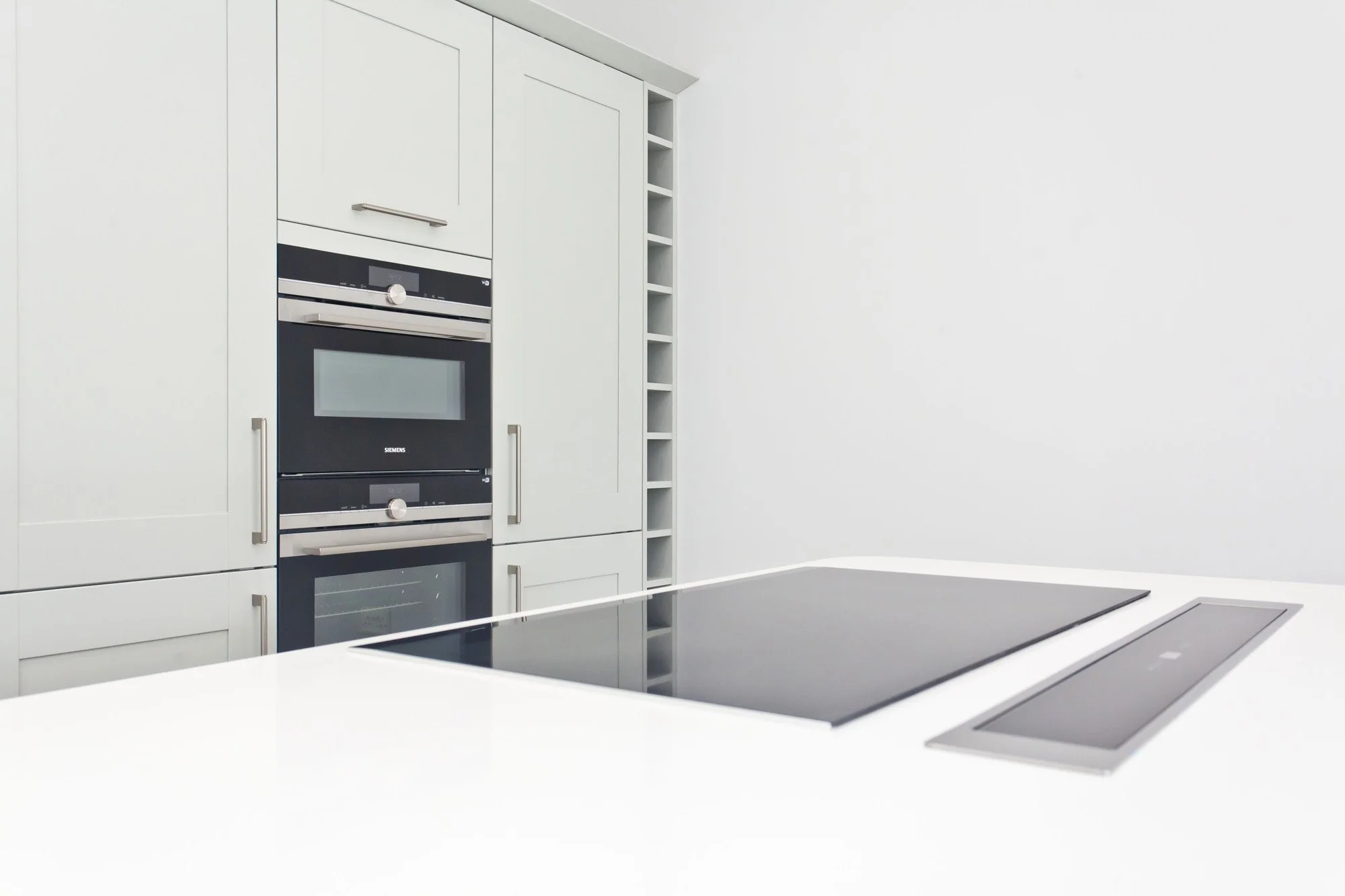 A modern kitchen with a white countertop, built-in Siemens oven, and a white wall with a vertical wine rack.