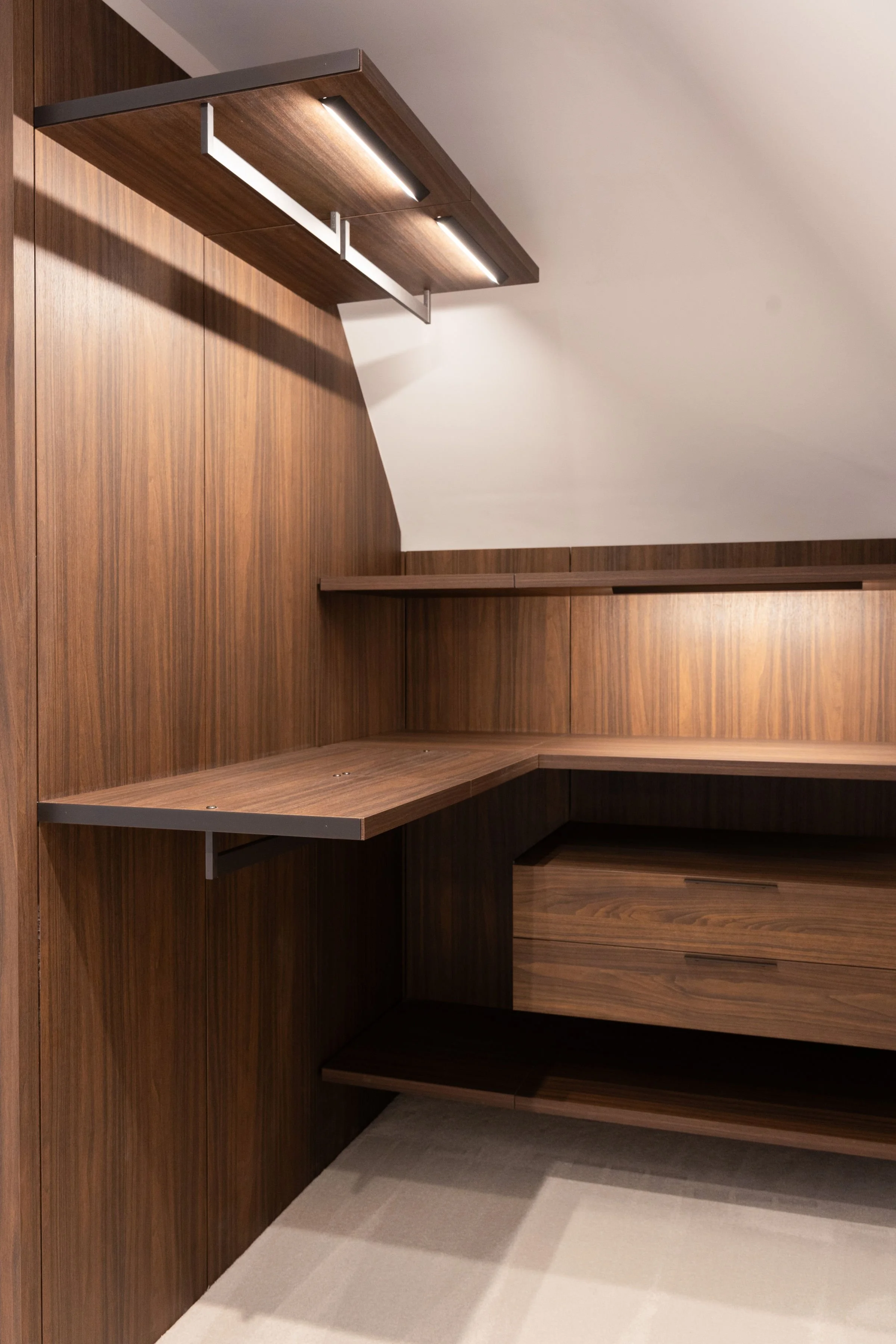 Corner of a room with wood-paneled walls and modern wooden shelving, illuminated by built-in ceiling lights.