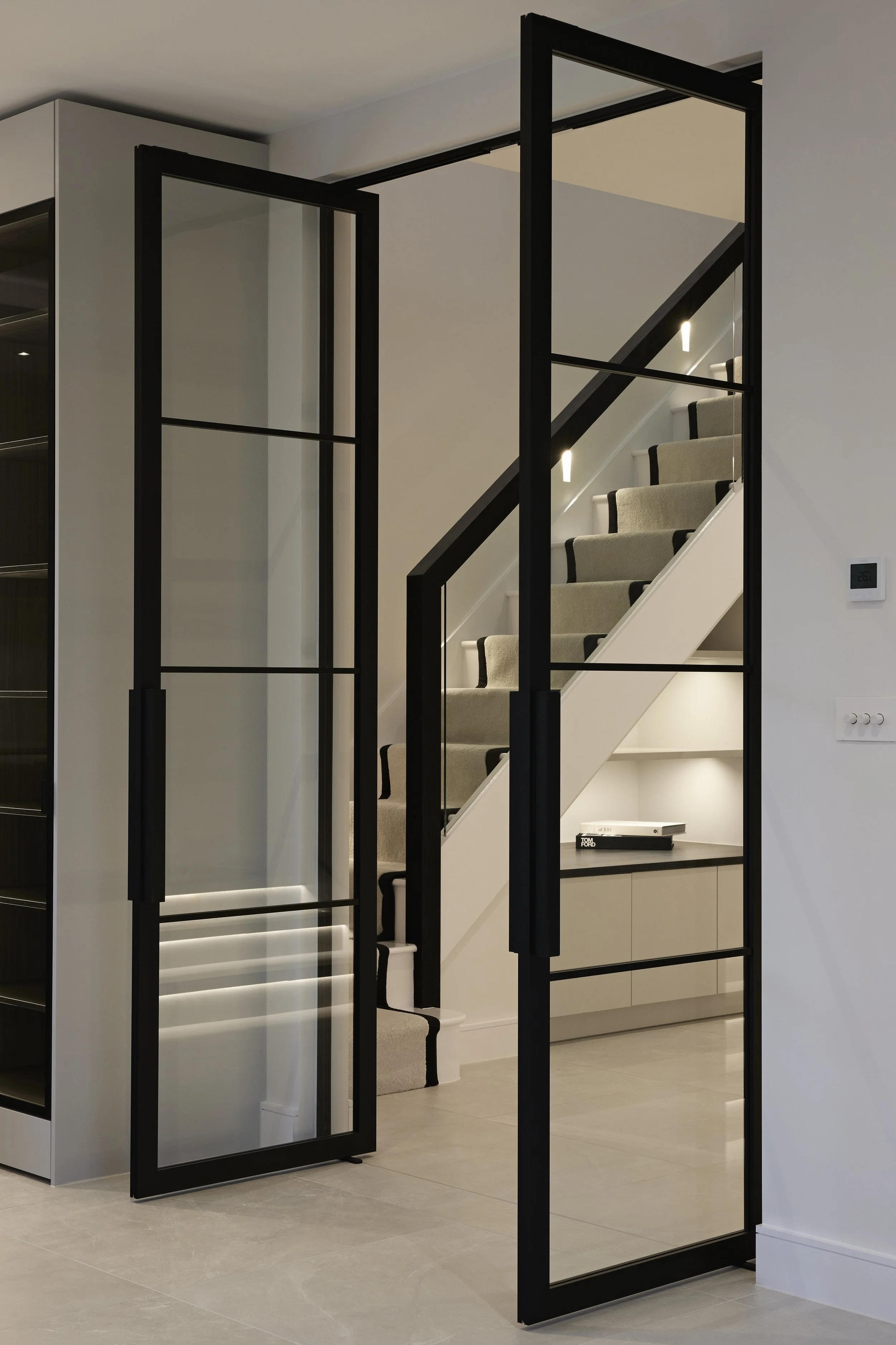 Modern interior with a staircase visible through black-framed glass doors.