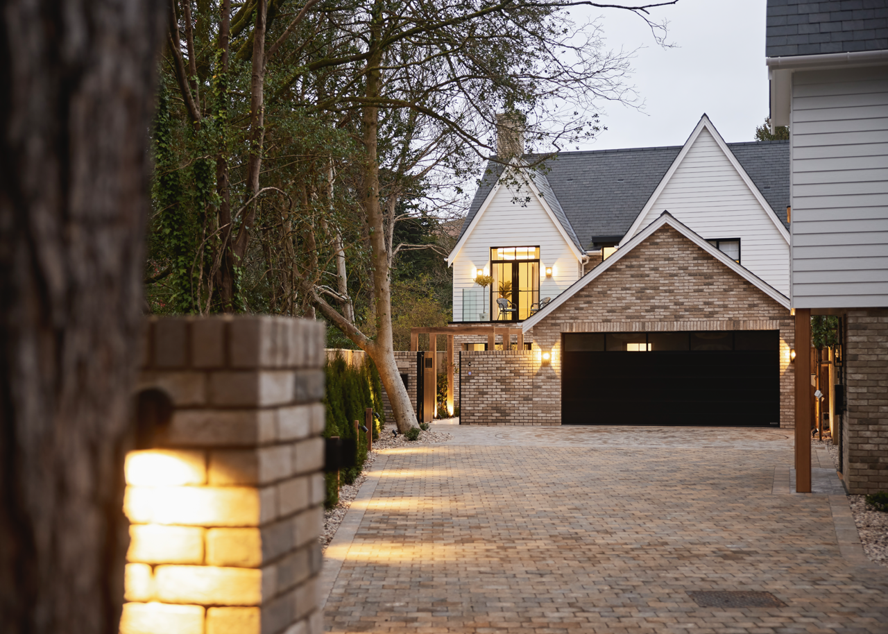 A modern house with a brick and white siding exterior, brick driveway, and outdoor lighting, at dusk.