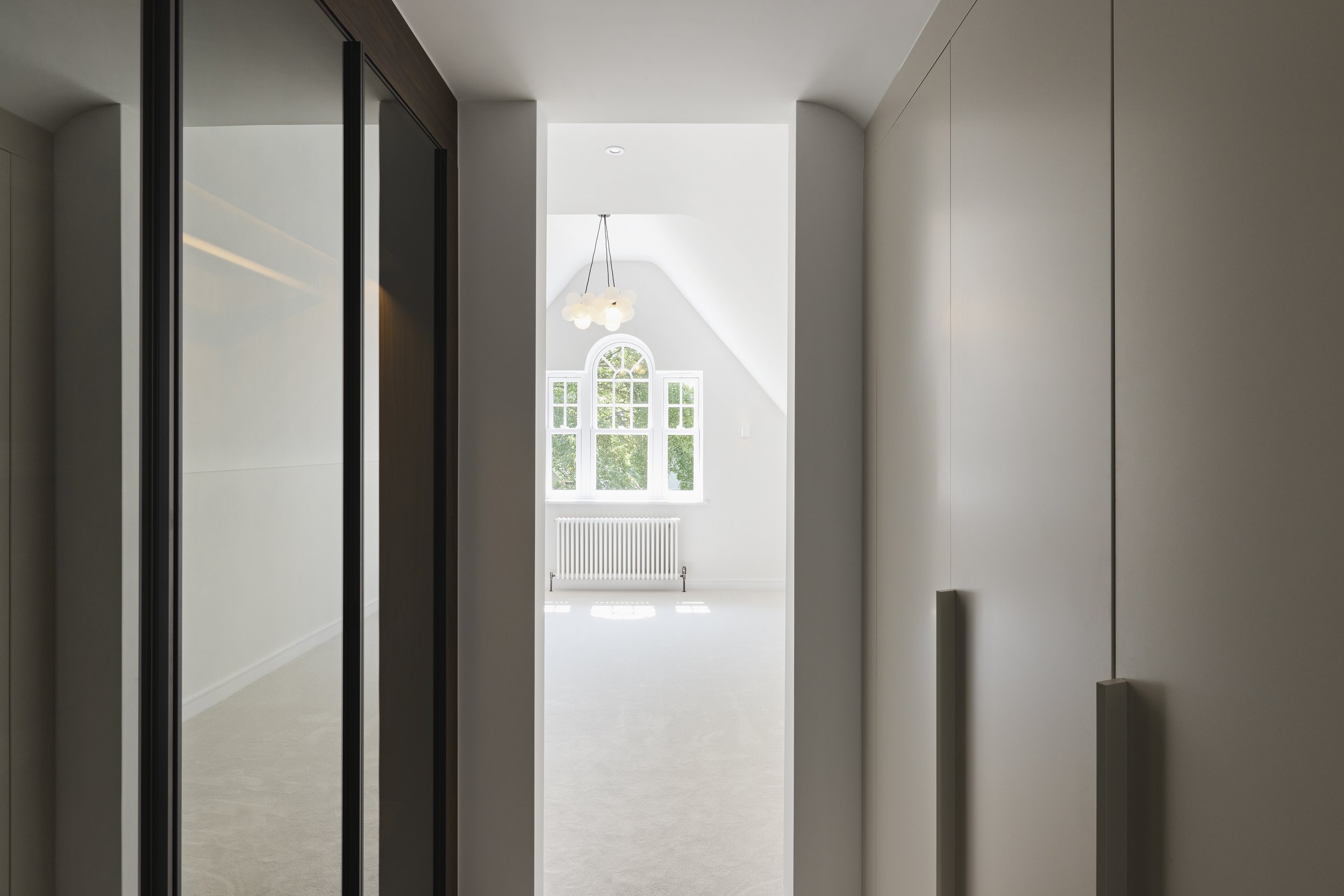 Interior view of a bright room with large windows and a modern hanging light fixture, seen through an entryway framed by sliding doors.