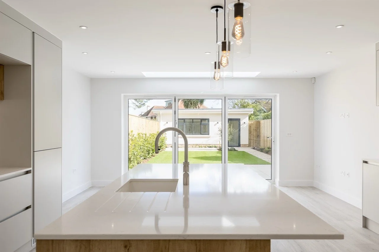 Modern kitchen with white countertops, a central island with a sink, and a large sliding glass door leading to a backyard.