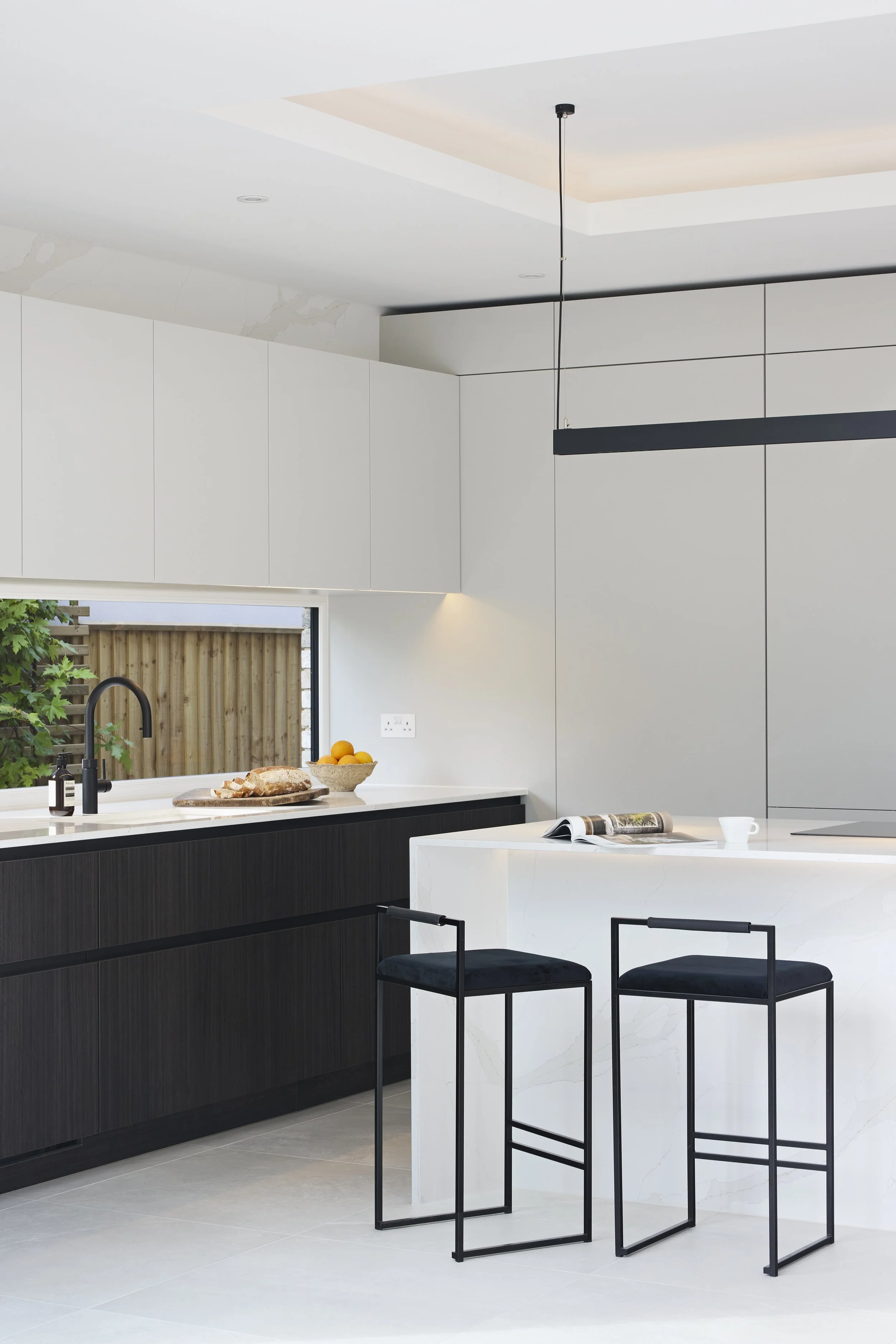 Modern kitchen with black and white cabinetry, white marble countertops, and black barstools with velvet seats.