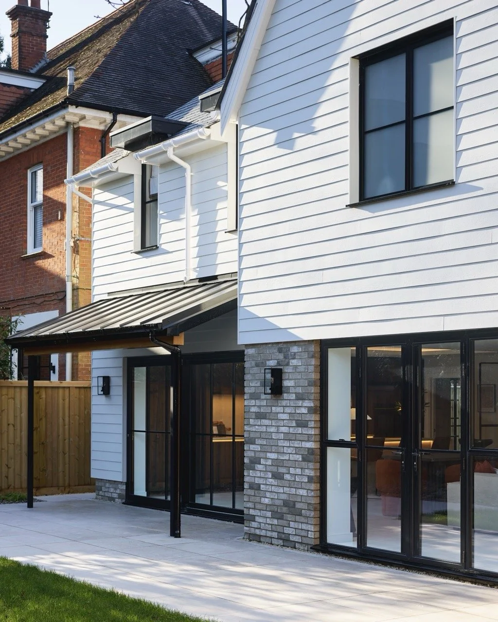 Modern two-story house in Bournemouth with white siding, large glass doors, black window frames, and a small covered patio area, surrounded by a wooden fence and a well-maintained lawn.