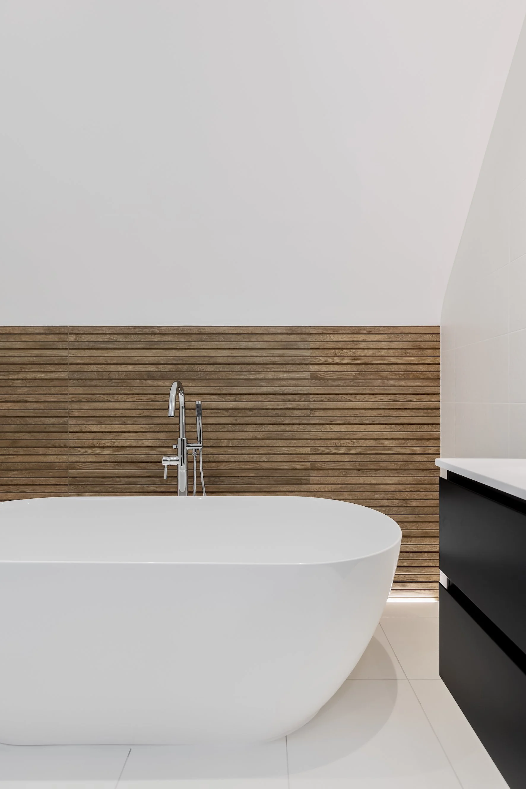 Modern bathroom with a freestanding bathtub, wooden wall paneling, white tiles, and a black vanity