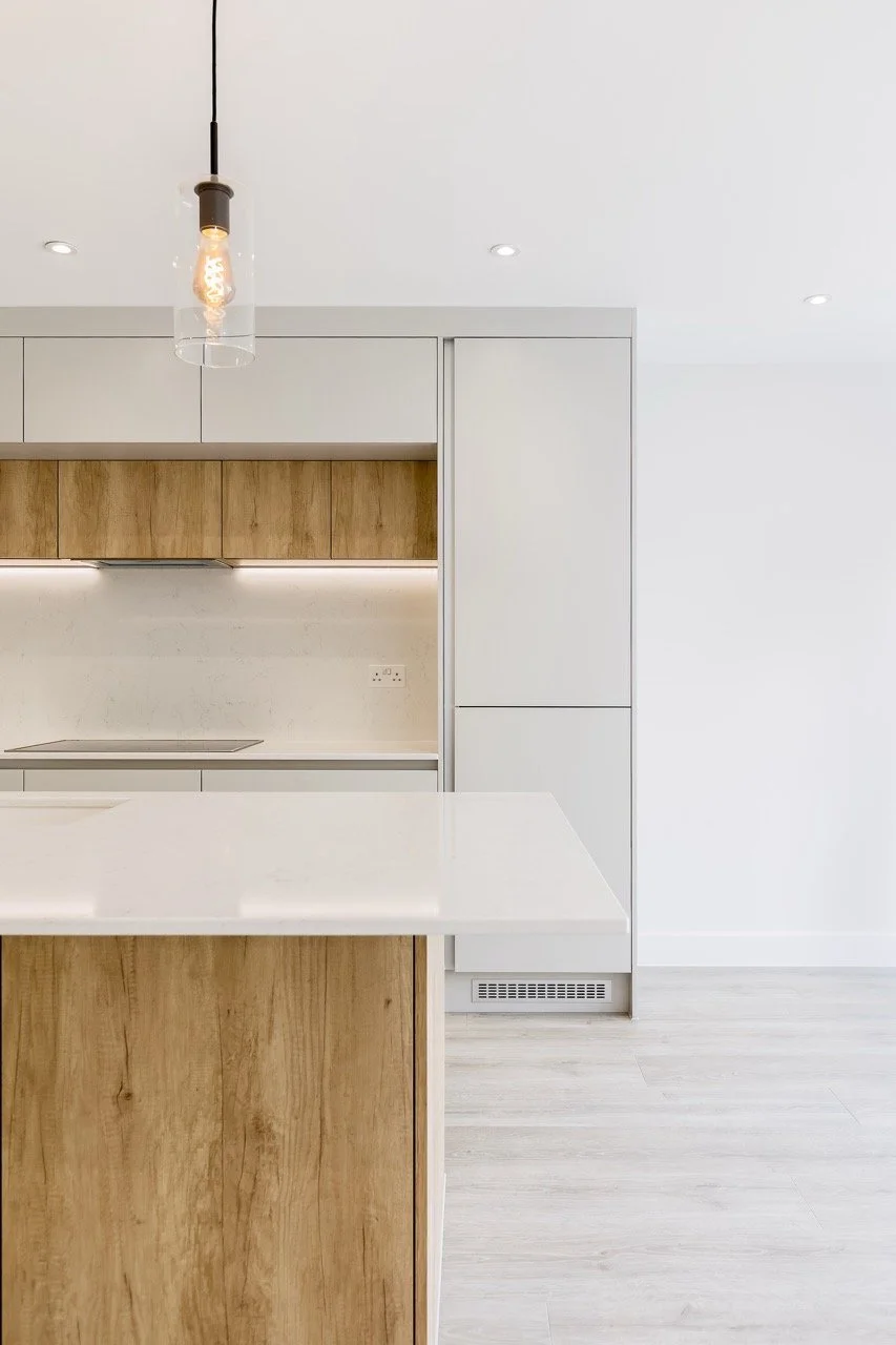 Modern kitchen with white cabinetry, wooden accents, a white countertop, and a glass pendant light.