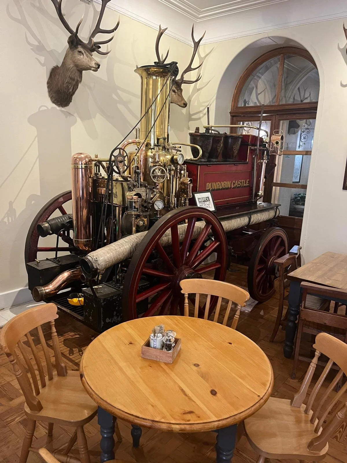 Decorative vintage fire truck display with a brass and wood design and mounted deer heads on the wall in a cozy, rustic room with wooden furniture.
