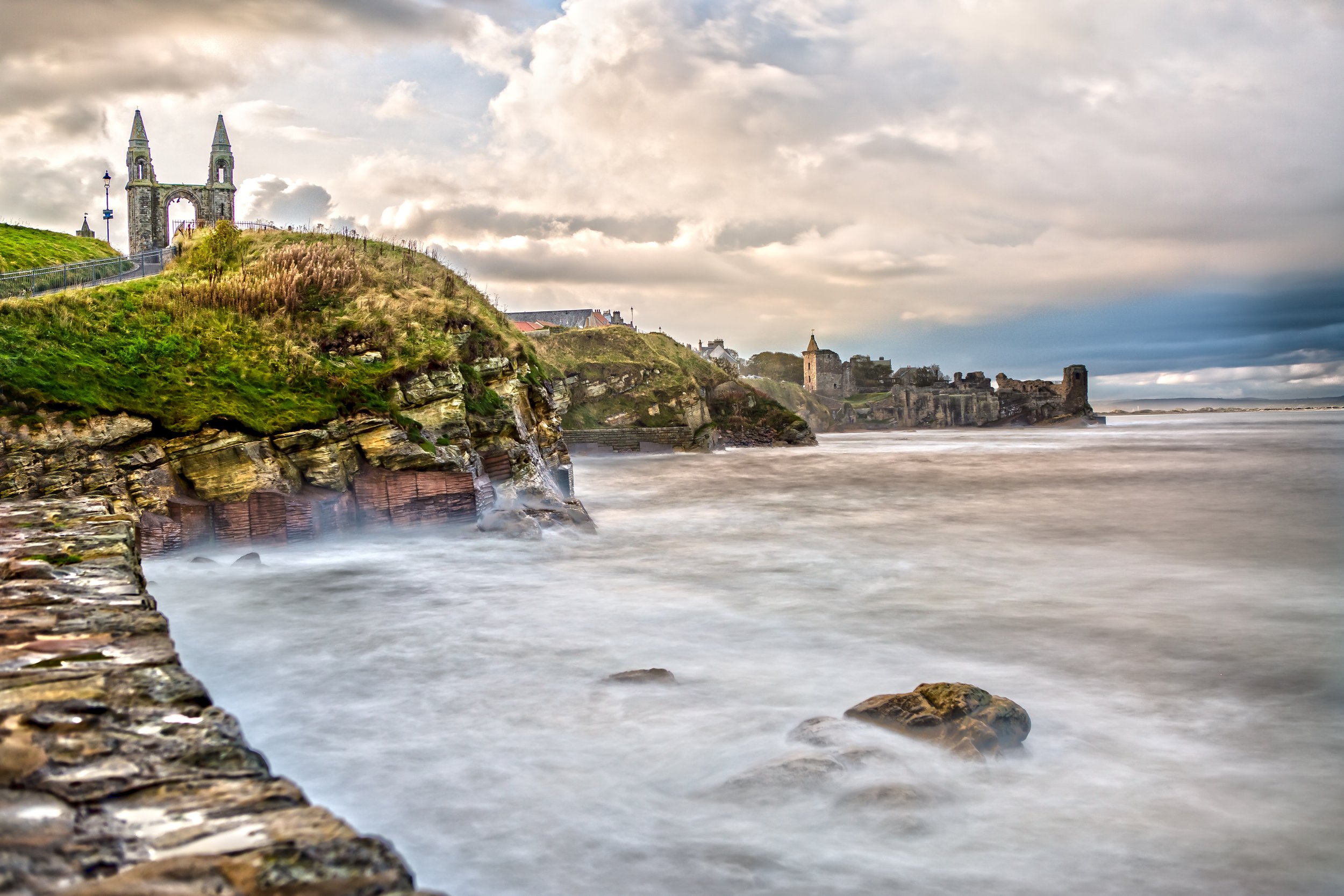 Cliffside with two church towers and ruins overlooking the ocean during cloudy weather