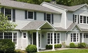 A large white two-story house with multiple windows and a covered front porch, surrounded by bushes and trees.