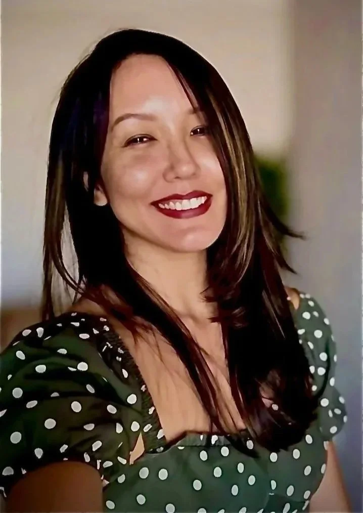 Mulher sorridente com cabelo castanho escuro e vestido verde com padrão de bolinhas brancas.