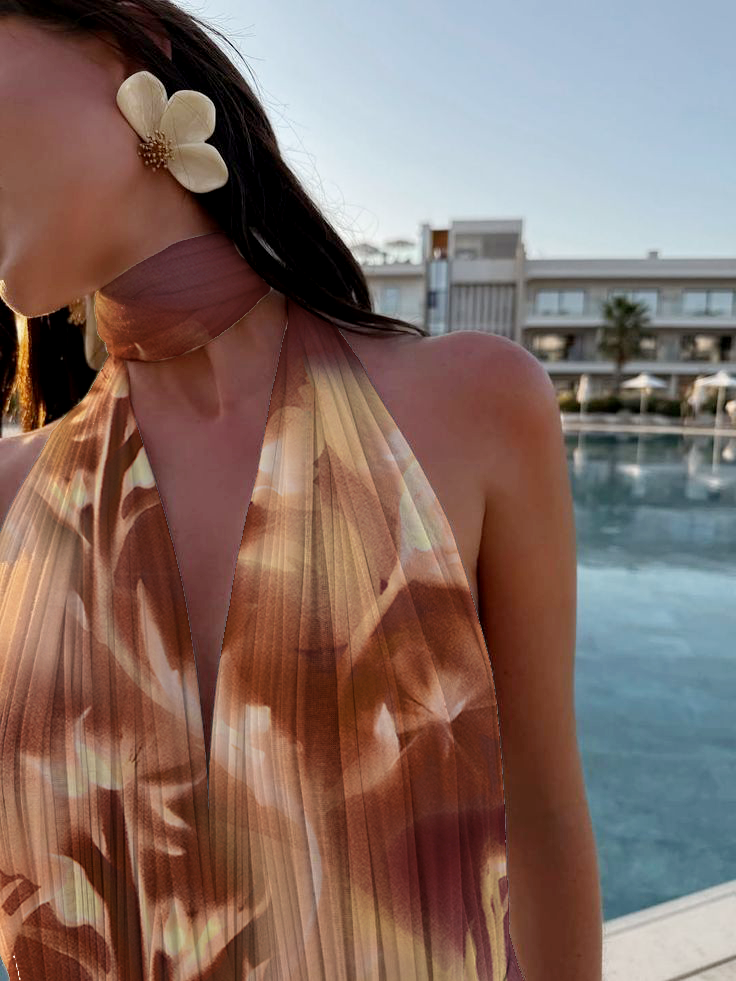 A woman wearing a flower-shaped earring and a pleated, patterned halter dress by a poolside with modern buildings in the background.