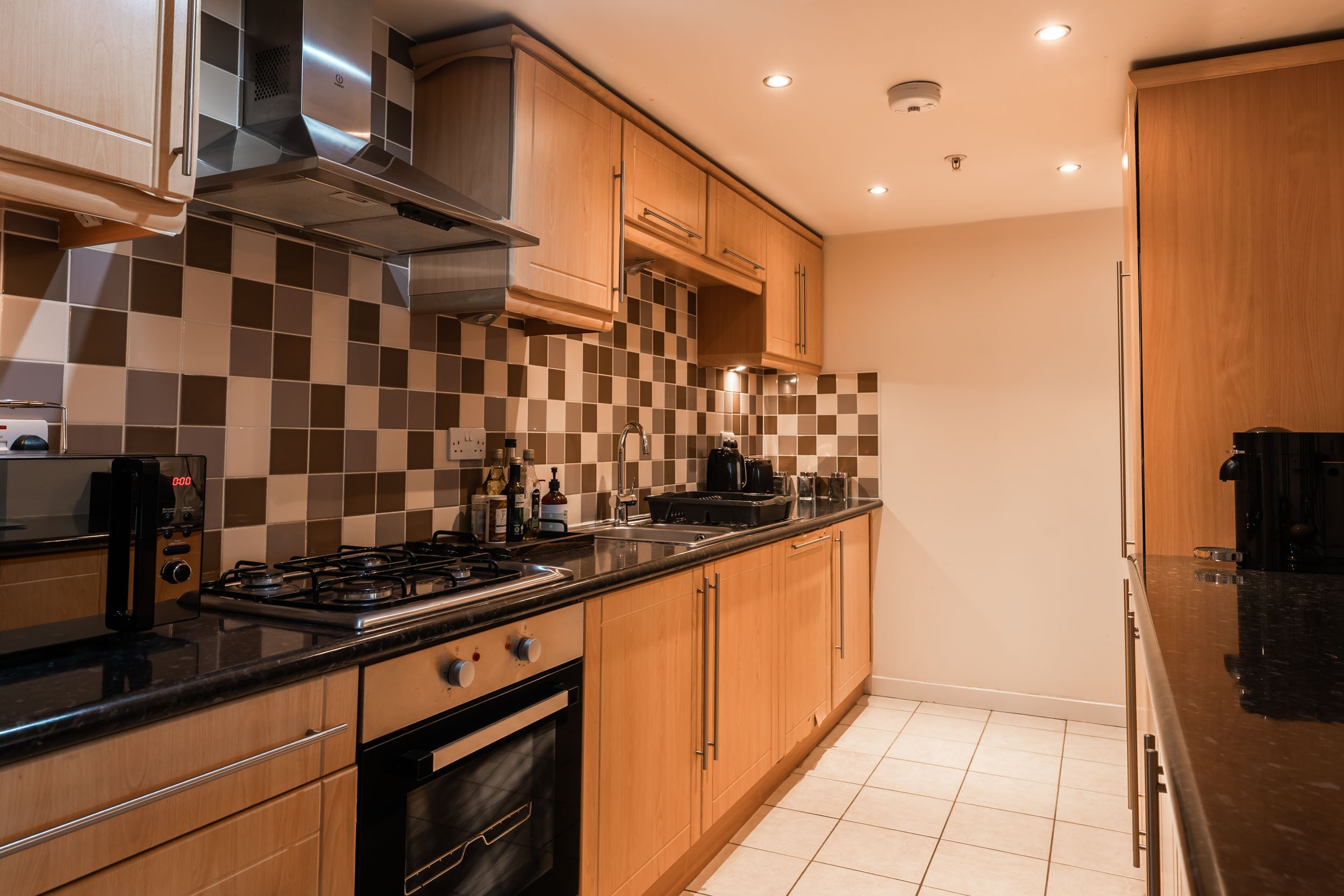 Kitchen with wooden cabinets, black countertops, beige tiled backsplash, and various appliances.