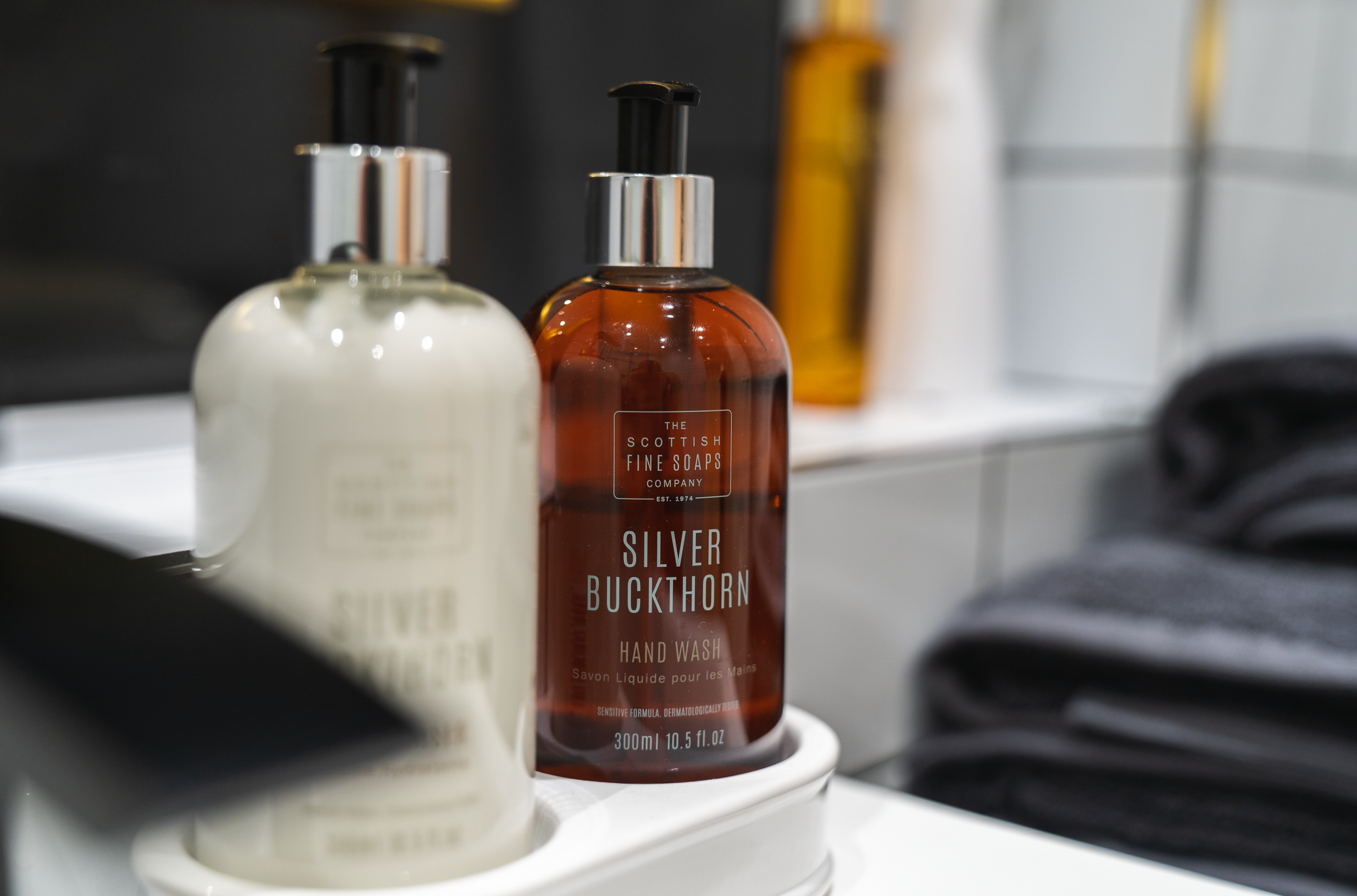 A bottle of Silver Buckthorn hand wash on a bathroom shelf, with other bottles and a towel nearby.
