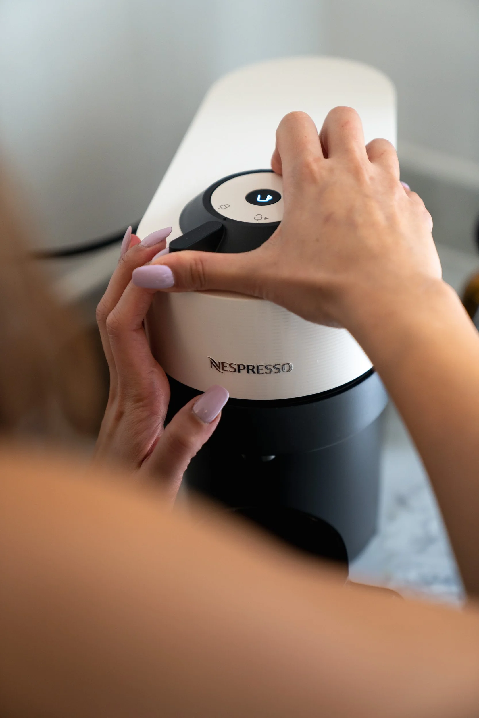 Close-up of hands adjusting a Nespresso coffee machine, with a focus on the machine's control dial.