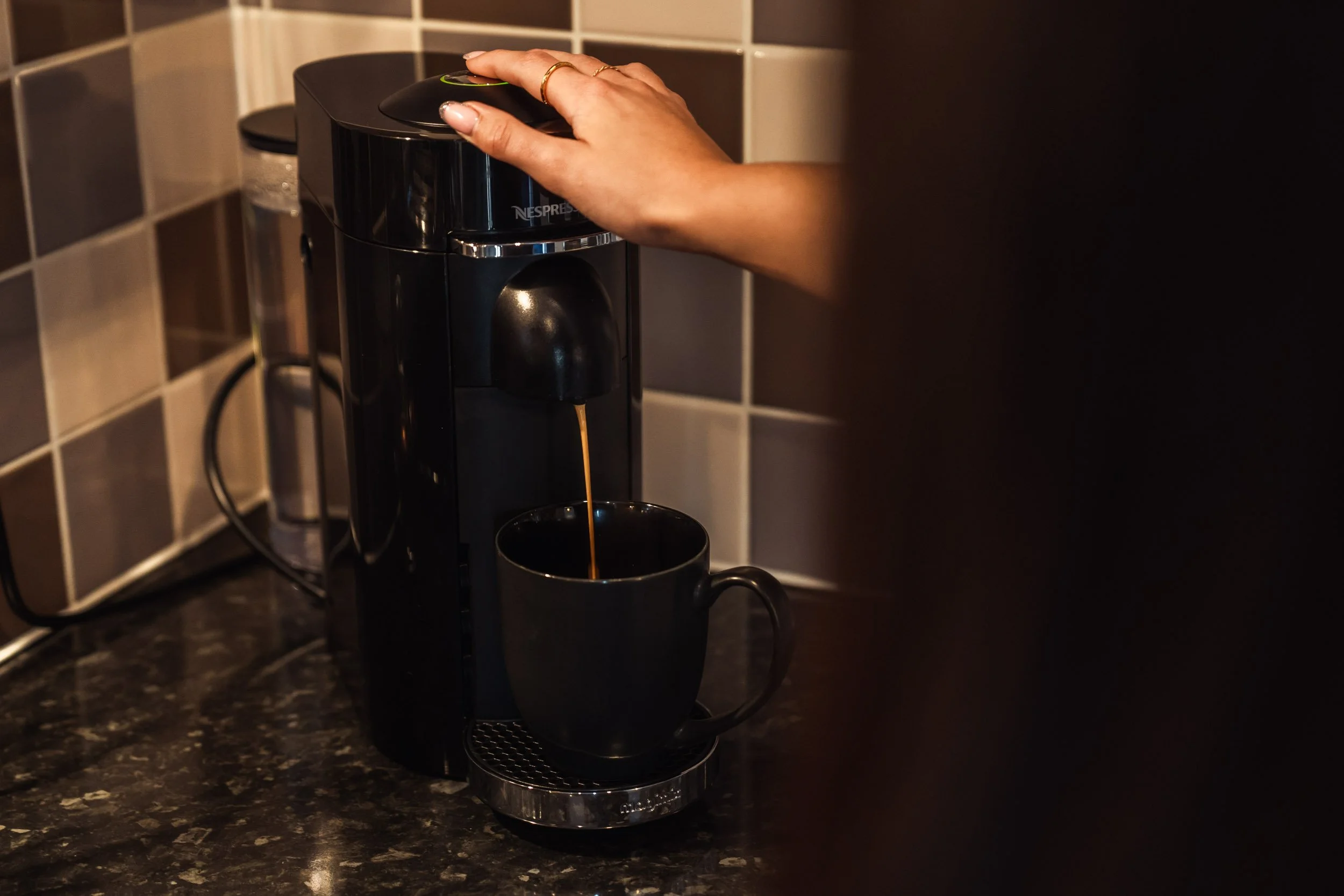 Person preparing coffee with a Nespresso machine, pouring coffee into a black mug on a kitchen countertop.